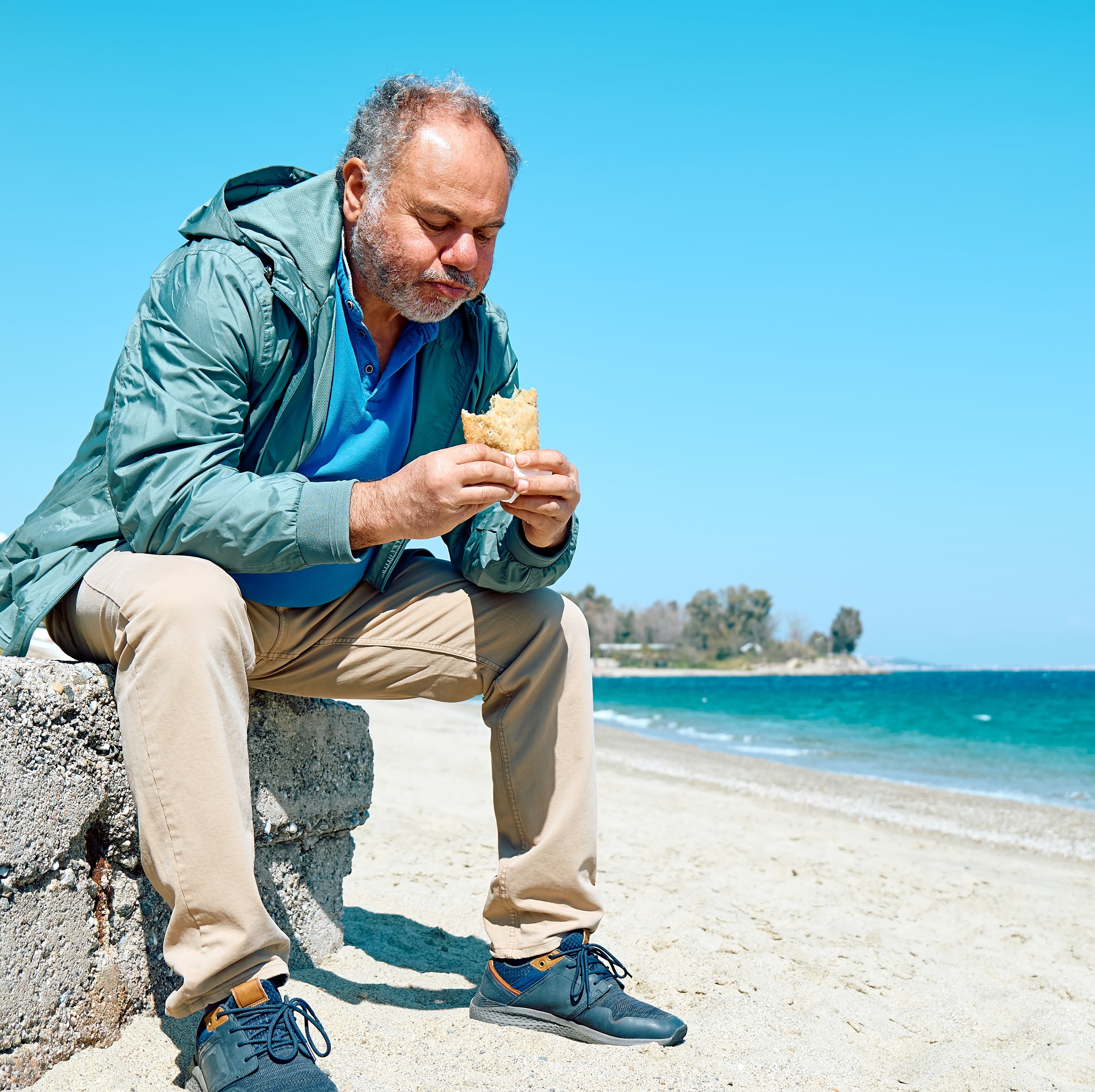 Bearded man eating on a park bench
