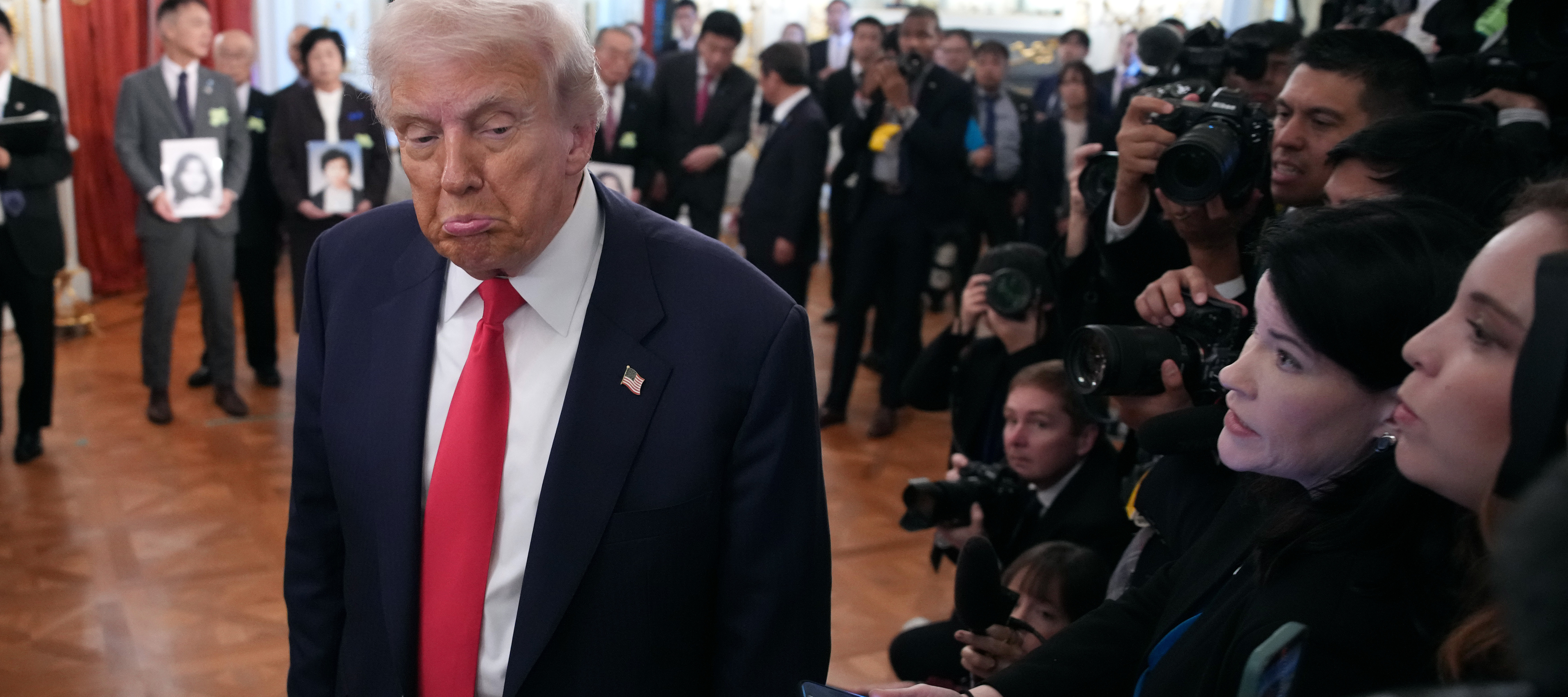 Donald Trump walks past reporters with a pouting expression.