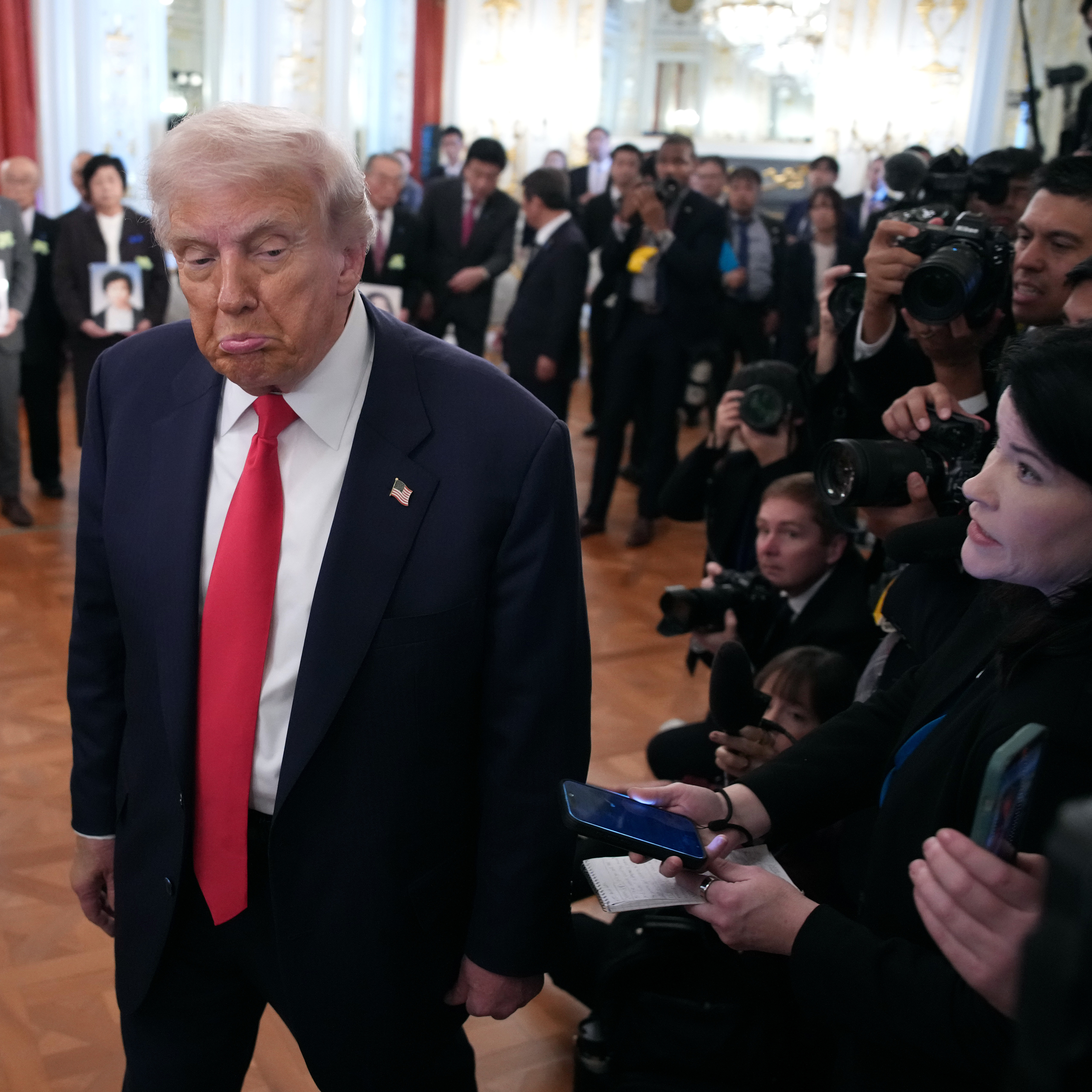 Donald Trump walks past reporters with a pouting expression.