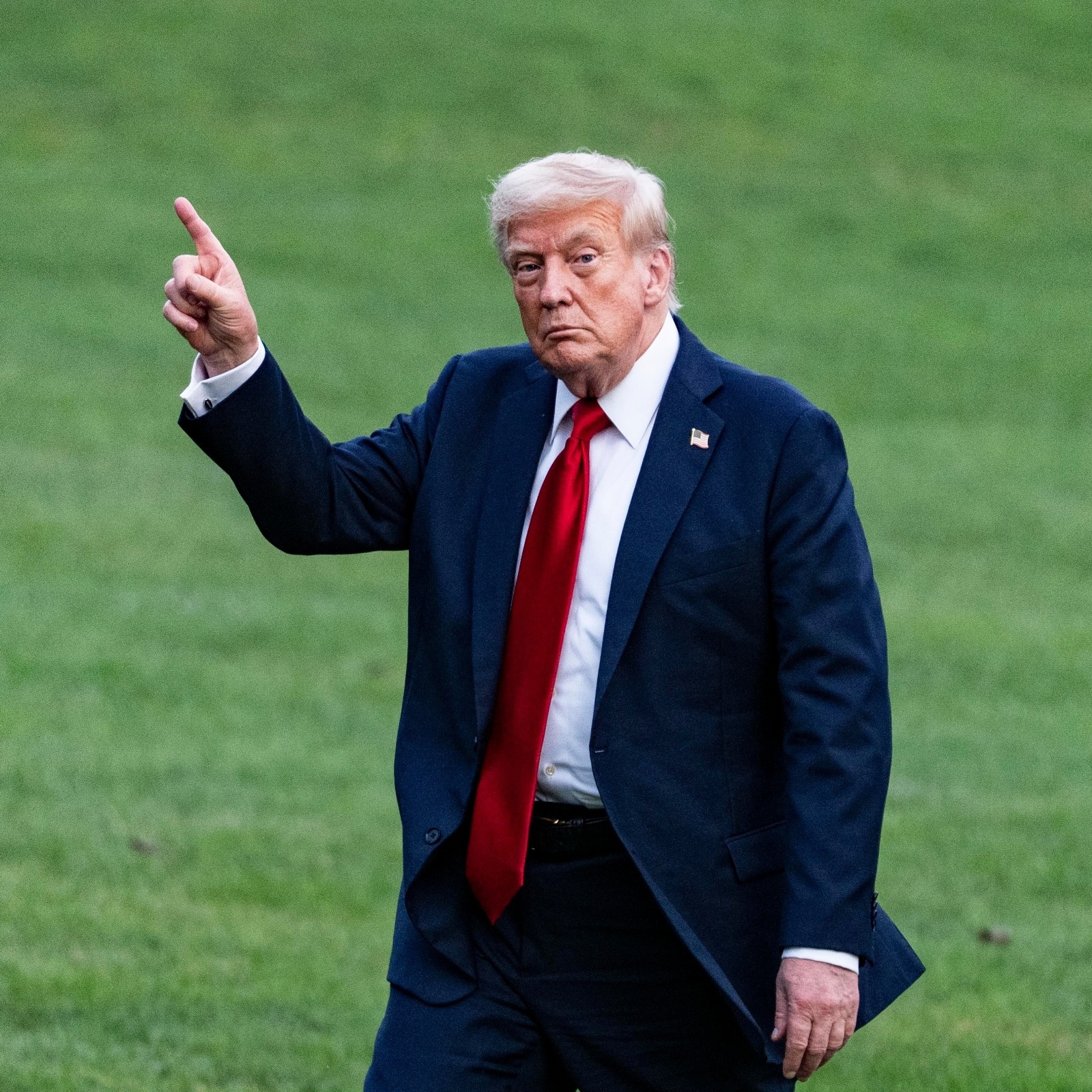 Donald Trump walking on a green lawn wearing a suit and pointing one finger in the air