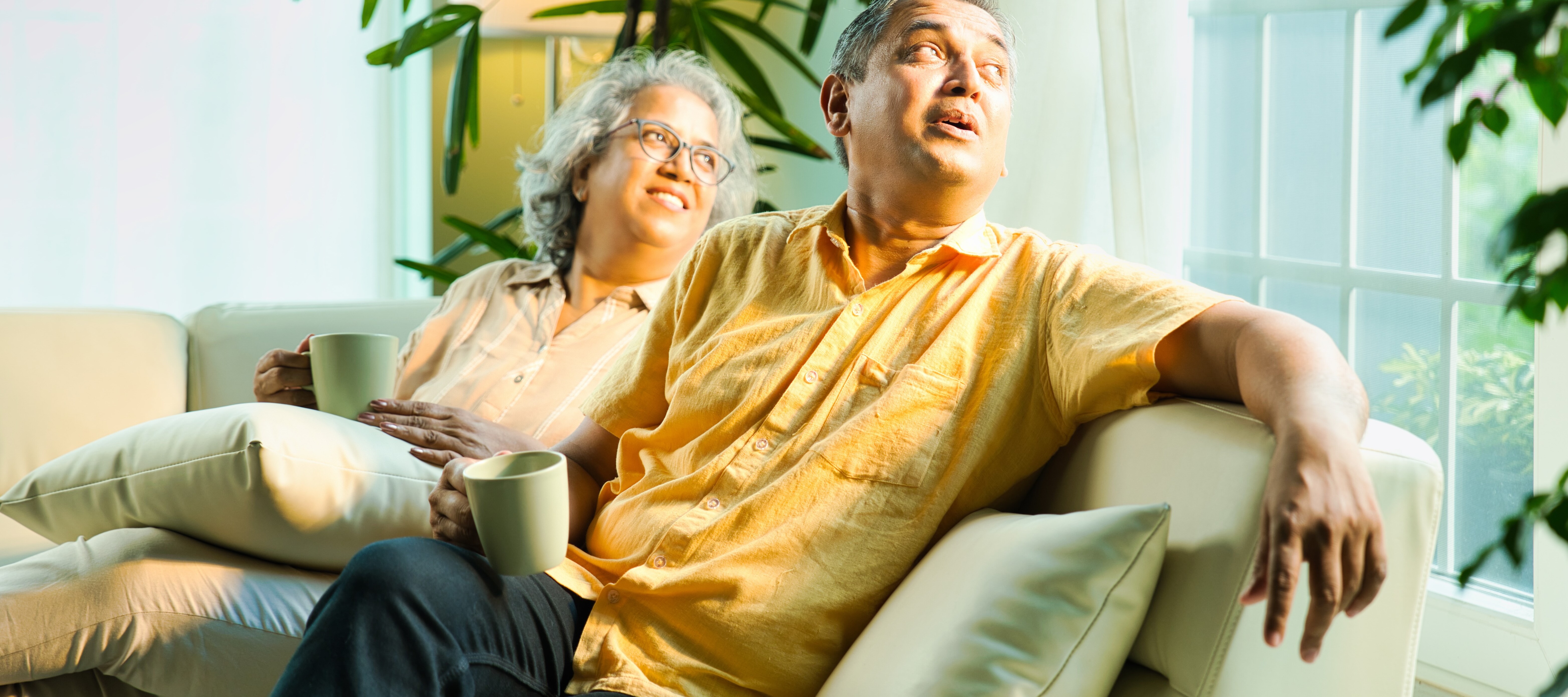 Older couple smiling on their couch, drinking coffee