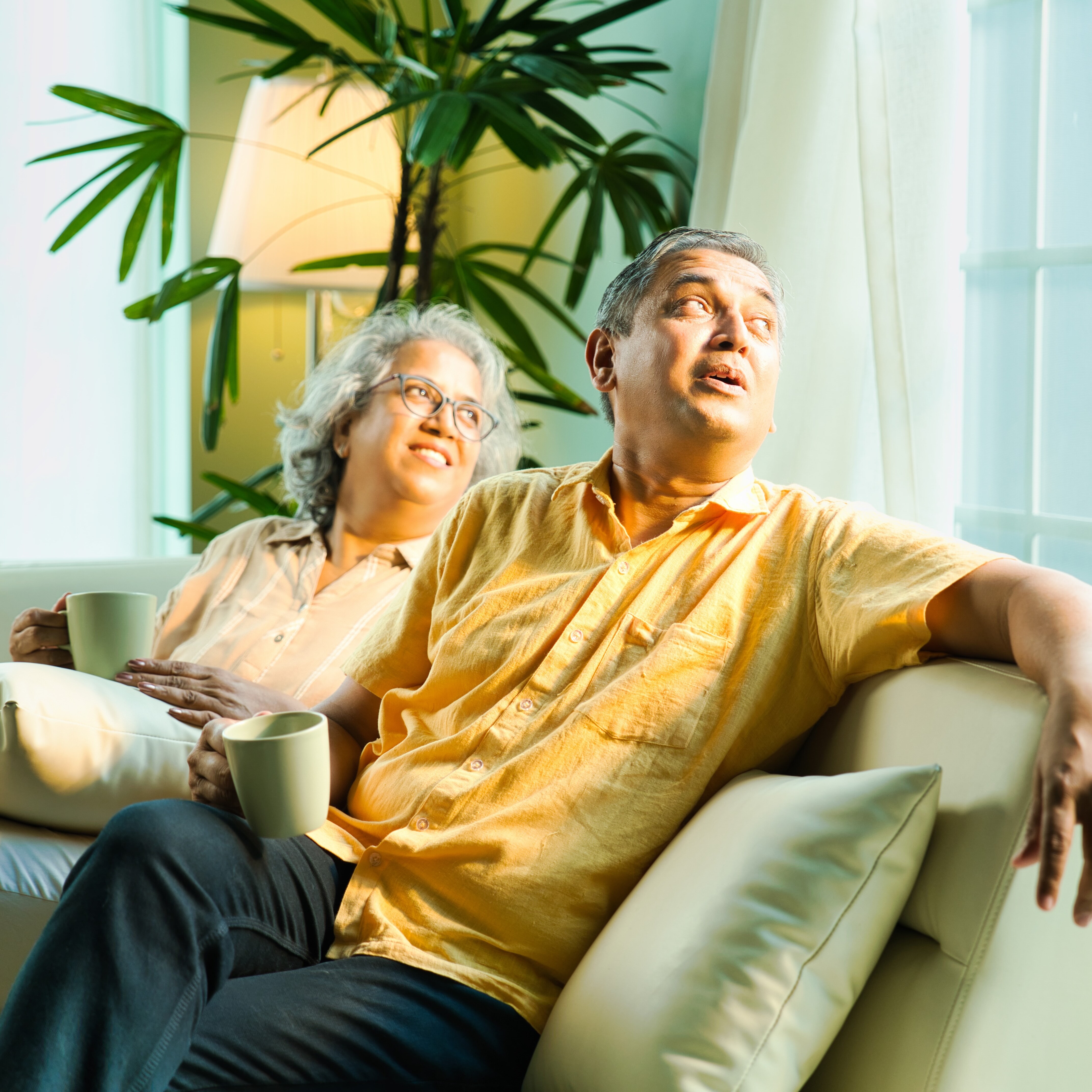 Older couple smiling on their couch, drinking coffee