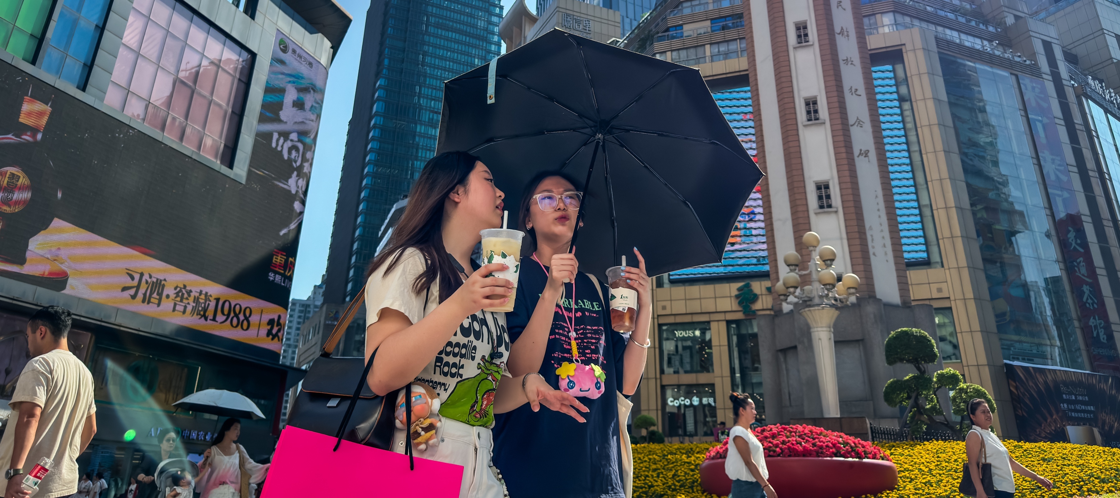 Two young women walk near the Jiefangbei Liberation Monument, a prominent landmark in Chongqing's central business district.