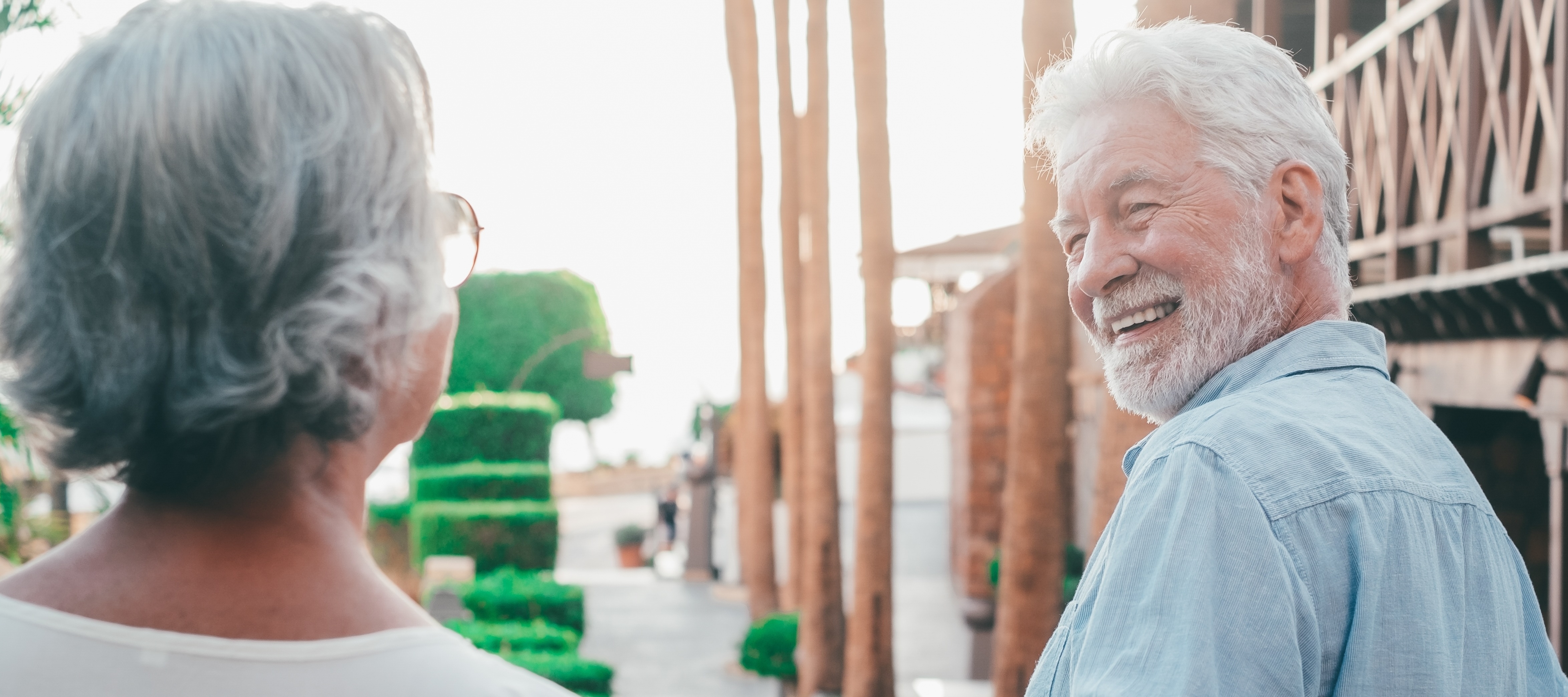 An older couple hold hands and walk down a street into the sunset.