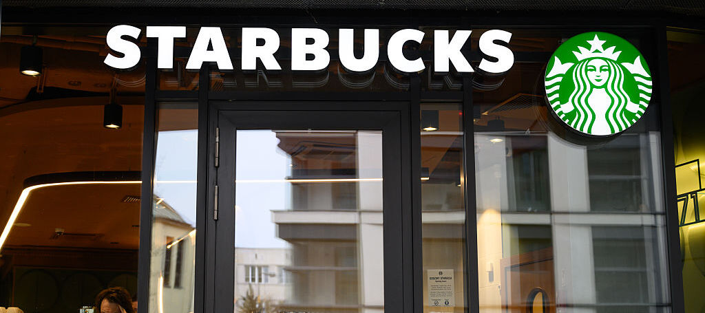 A photo of the Starbucks logo with a man working on a laptop