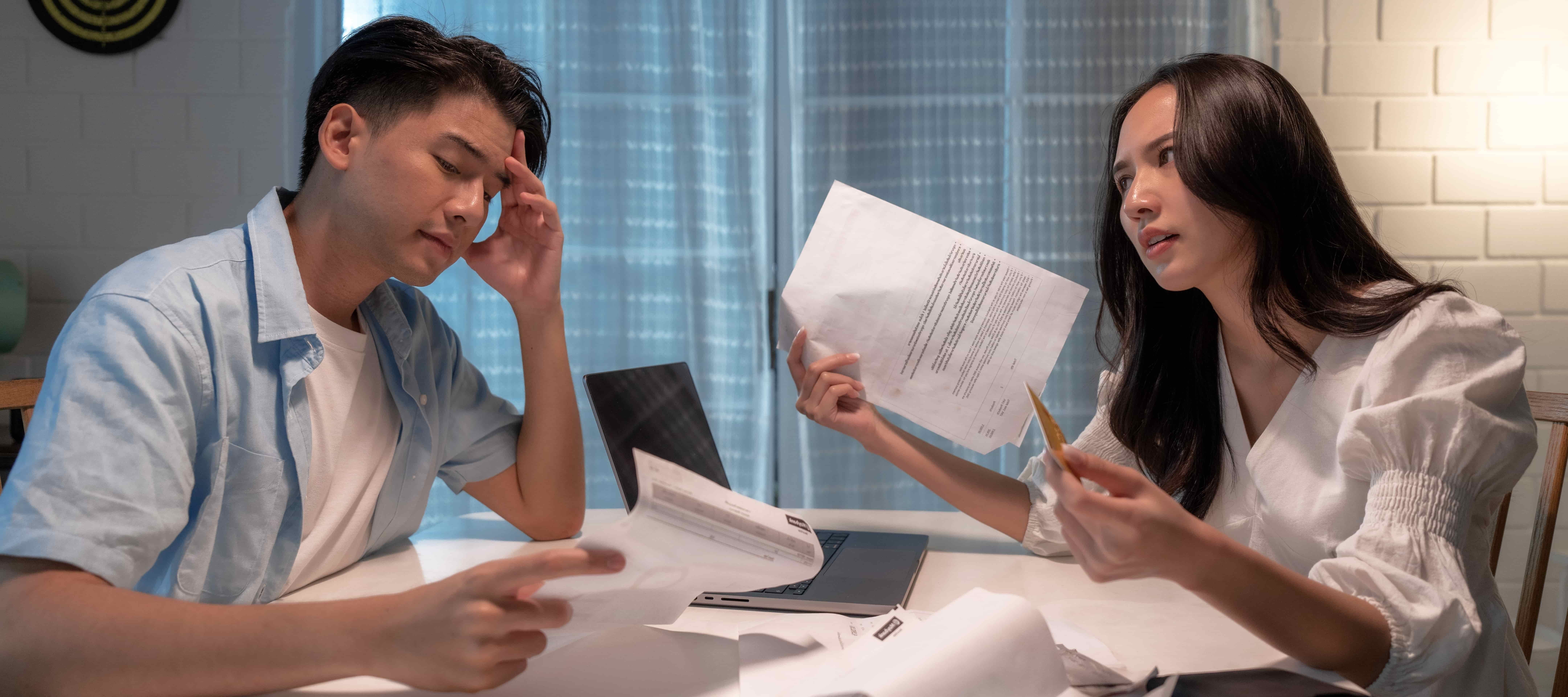 A photo of a visibly stressed man and a frustrated woman reviewing their finances together.