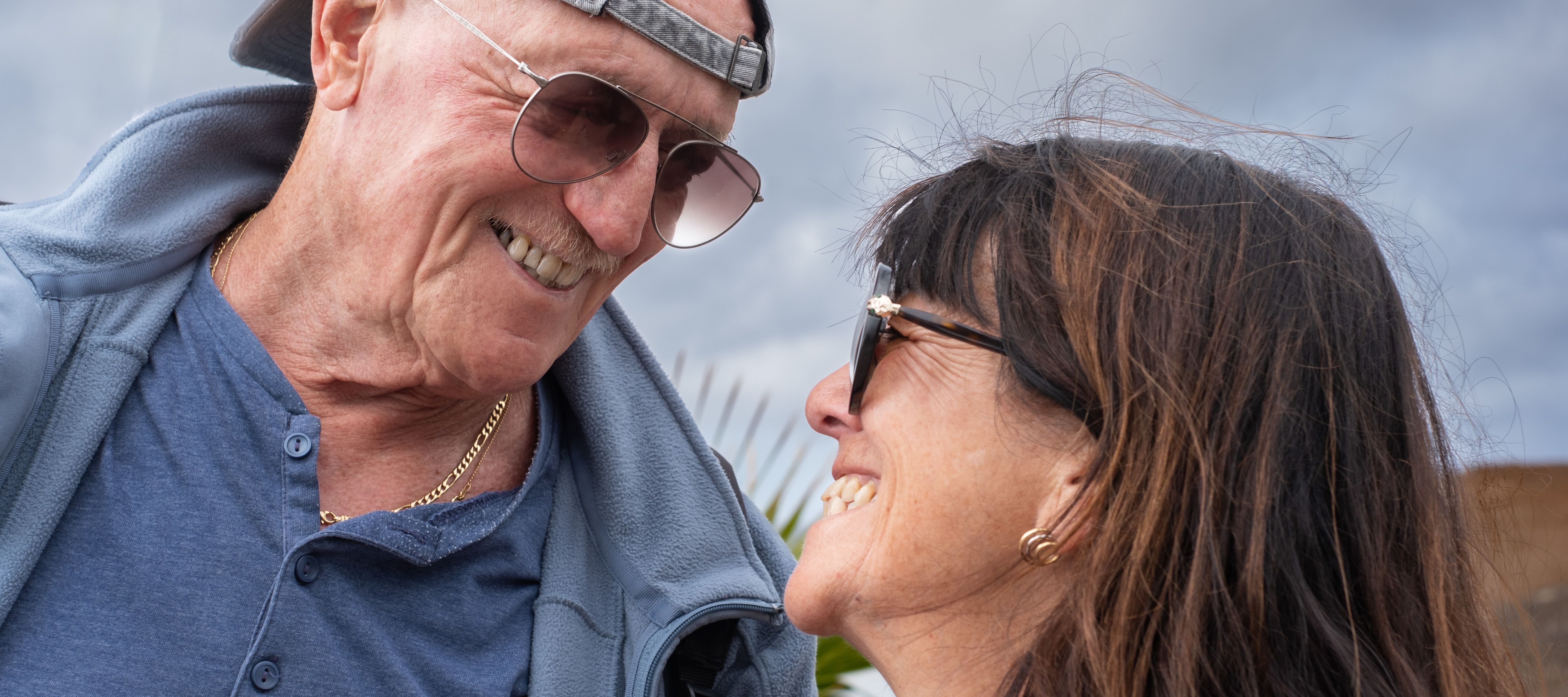 An octogenarian with a backwards hat looking at his daughter, with both smiling.