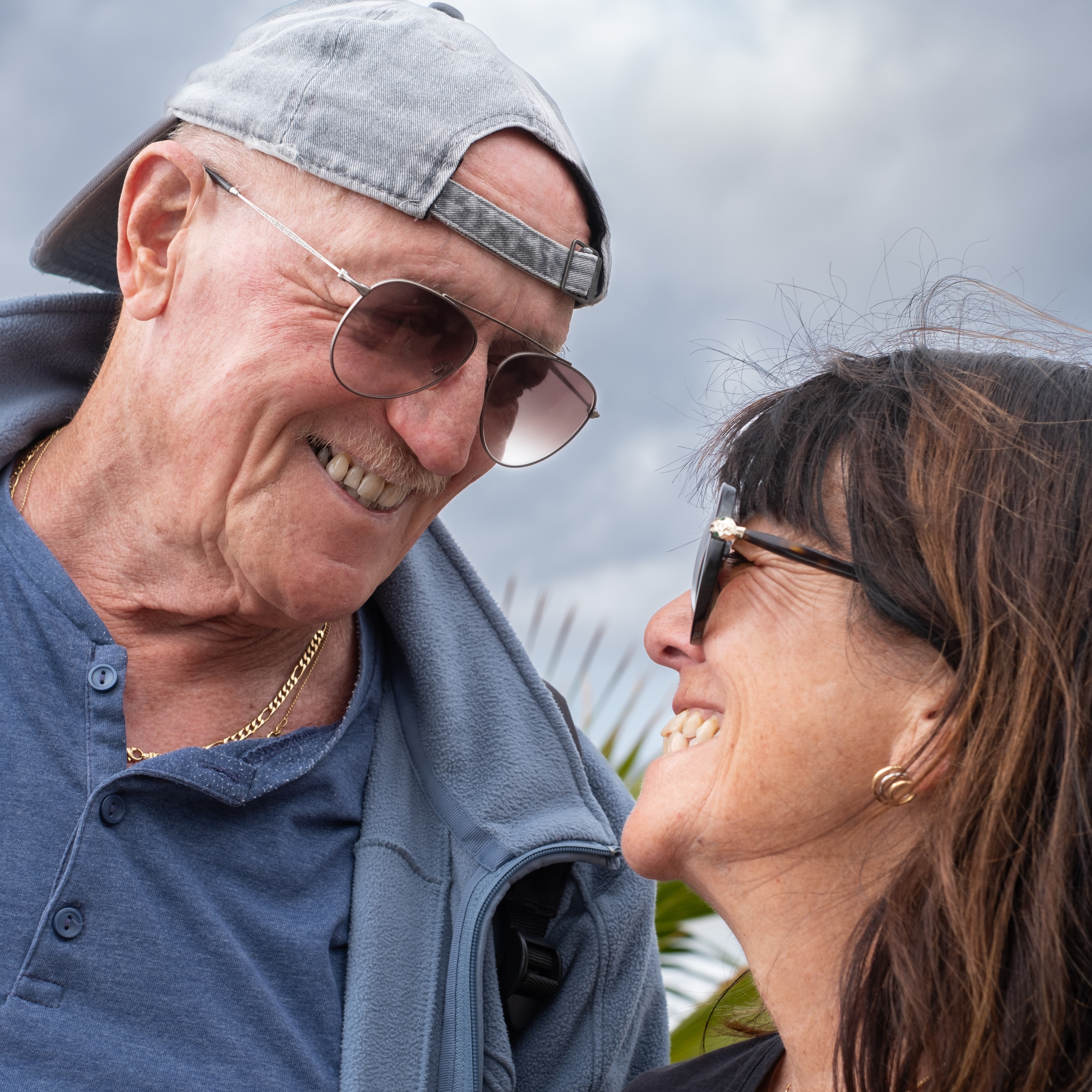 An octogenarian with a backwards hat looking at his daughter, with both smiling.
