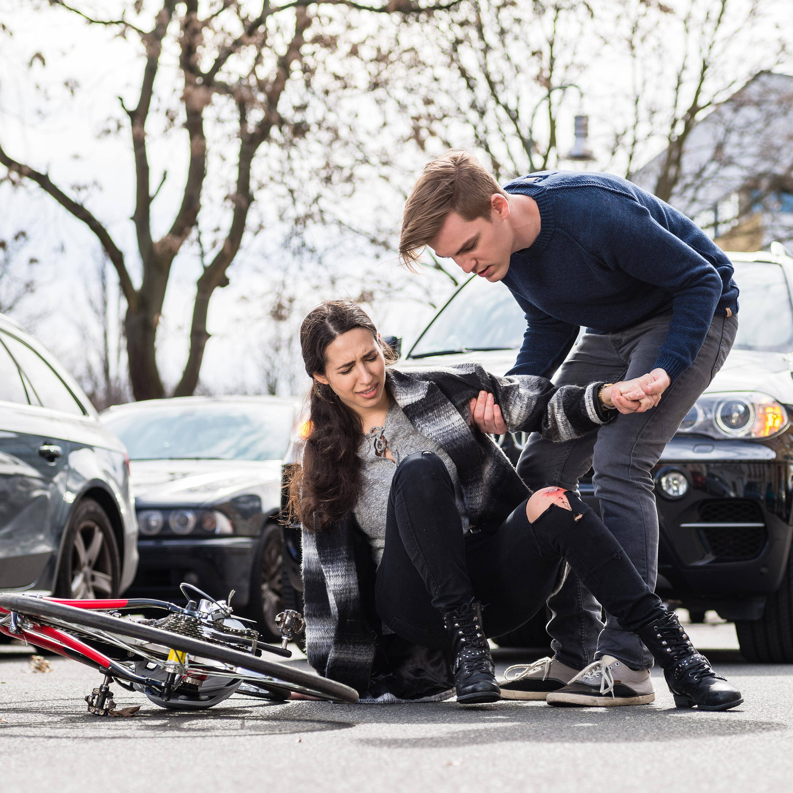 A young man helps a young female cyclist up after getting hit by a car.