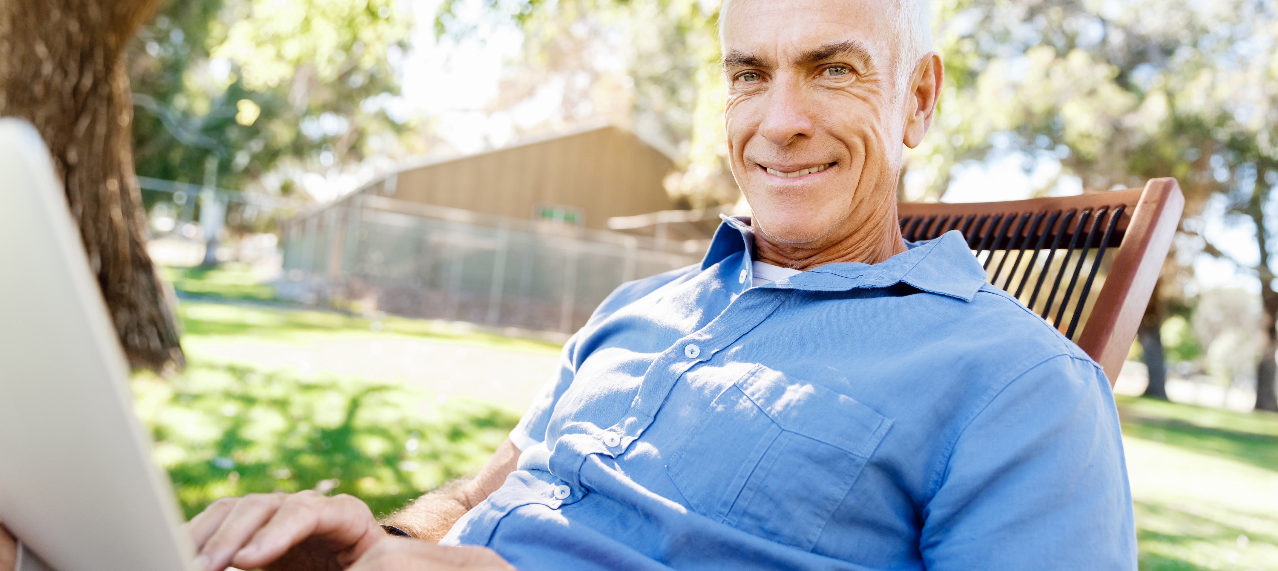 A man looking with his laptop on a chair outside in beautiful weather.