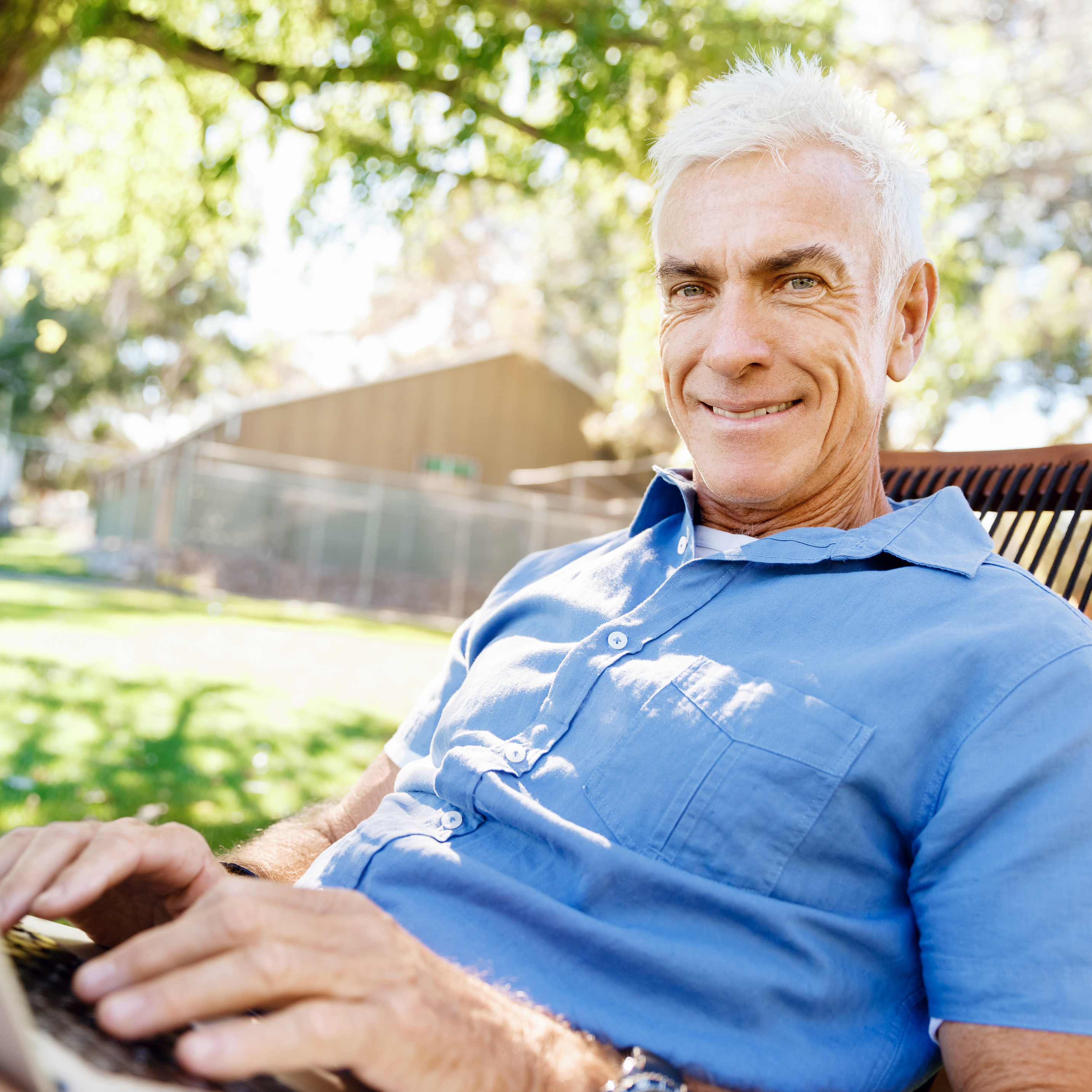 A man looking with his laptop on a chair outside in beautiful weather.