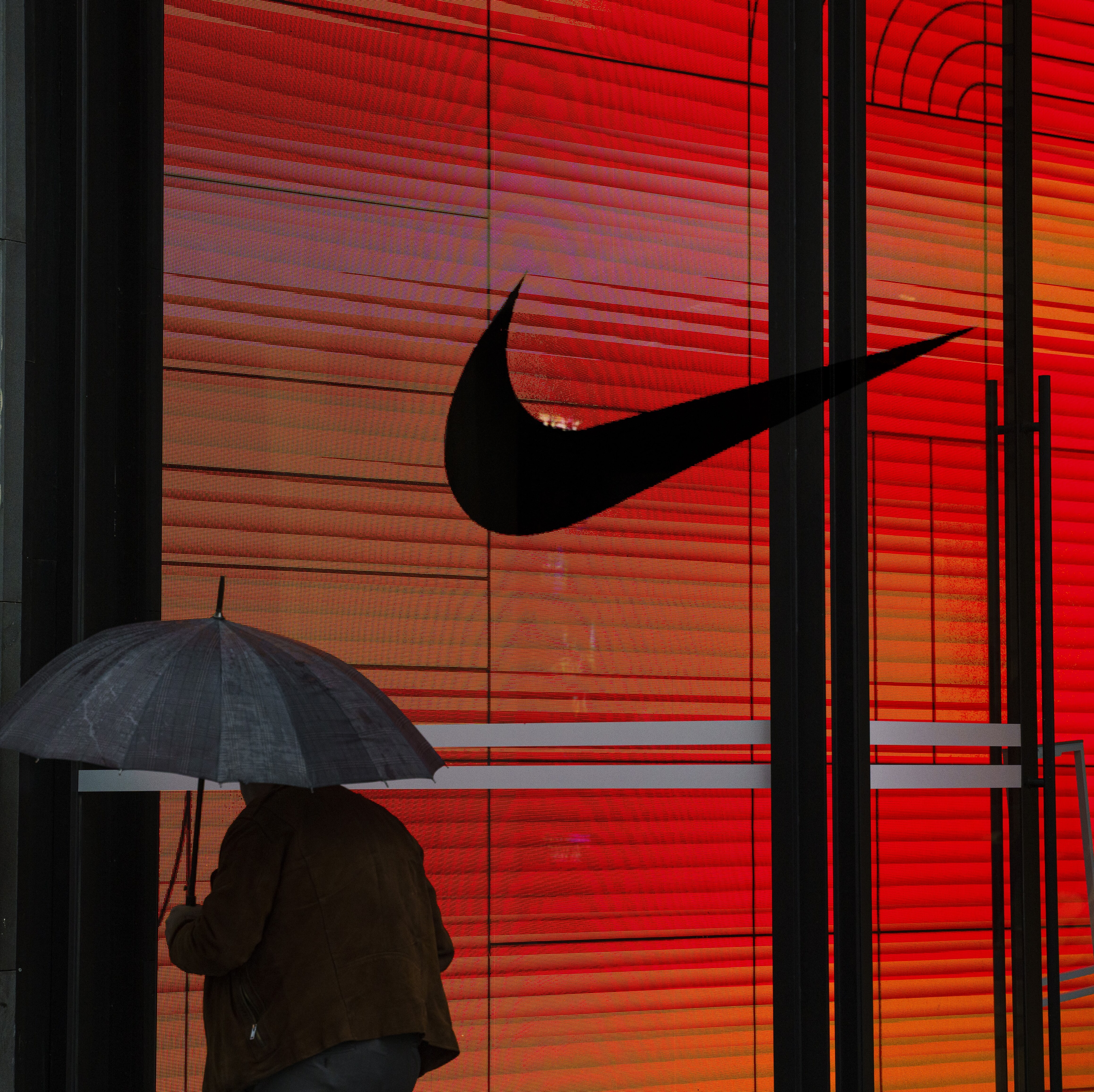 Nike, its logo scene here on a storefront as a person carrying an umbrella walks past, recently made its second round of job cuts in 2026, laying off 1,400 employees..