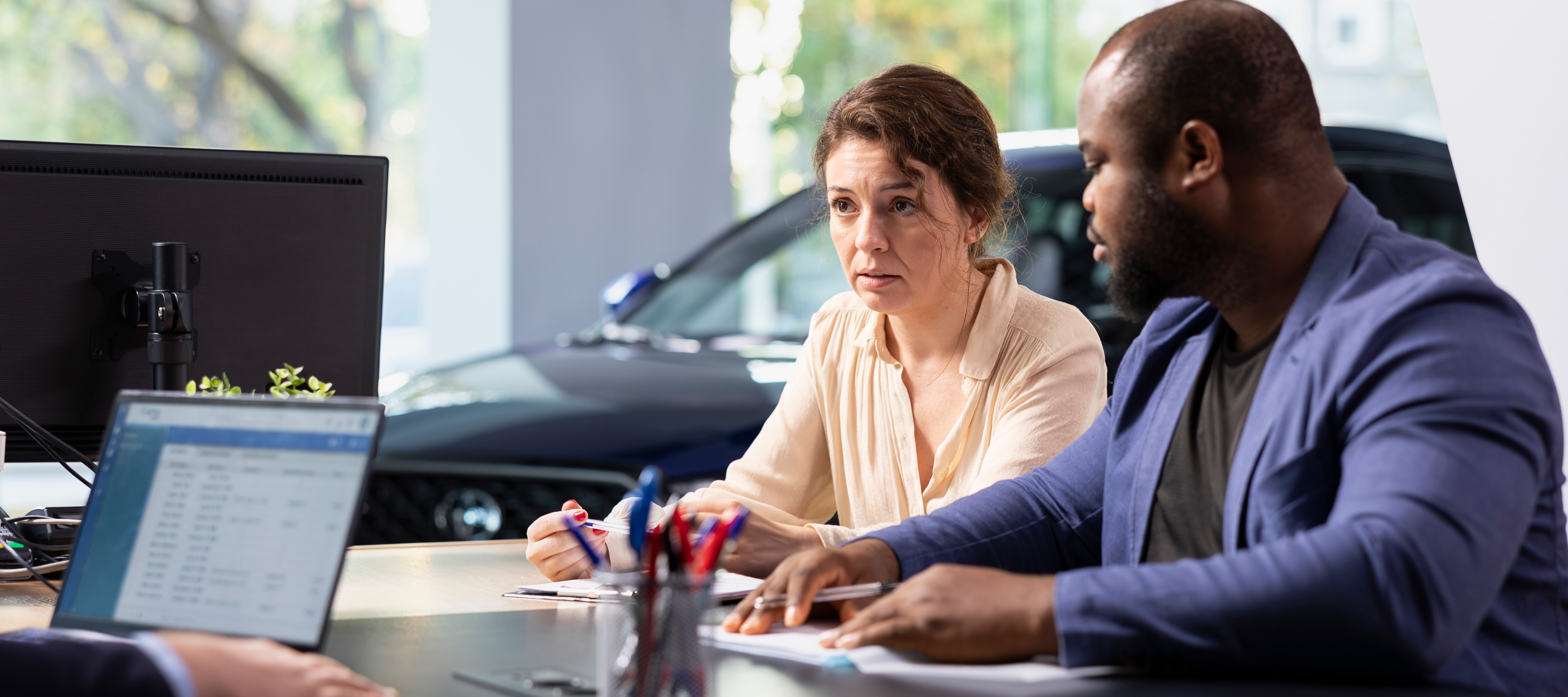A couple in a car showroom talk to a car salesman about pricing on a car.