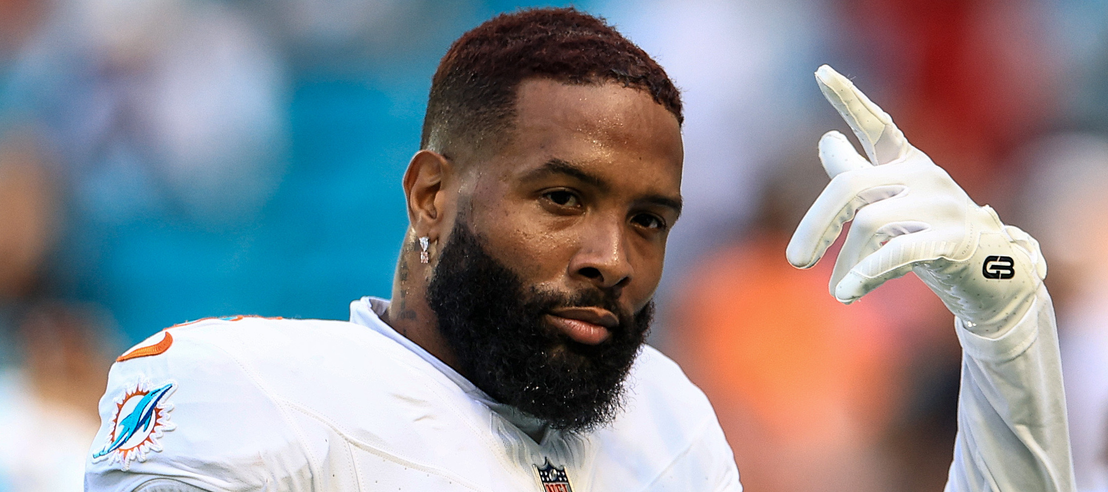 Odell Beckham Jr. throws up one hand while smiling slyly at the camera.