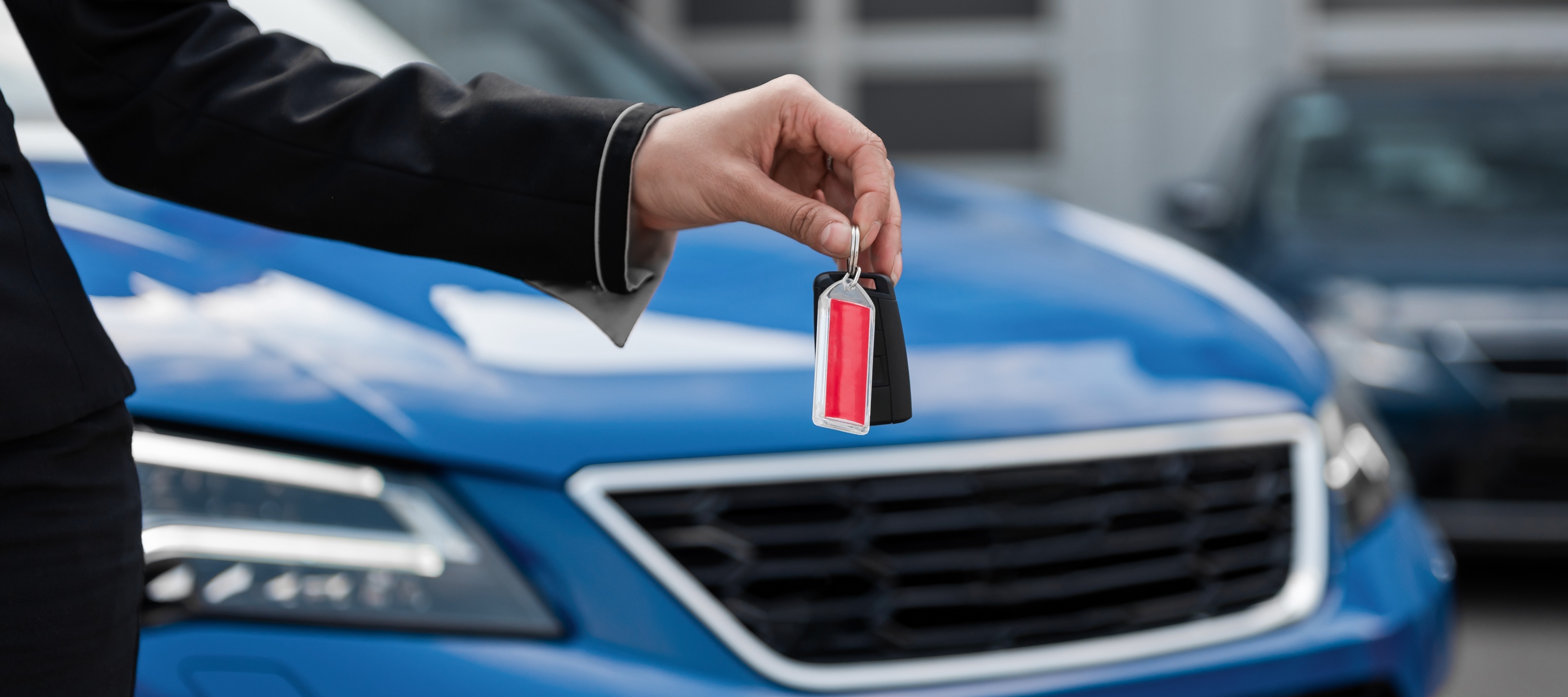 A woman holding out a set of car keys with a blue car in the background