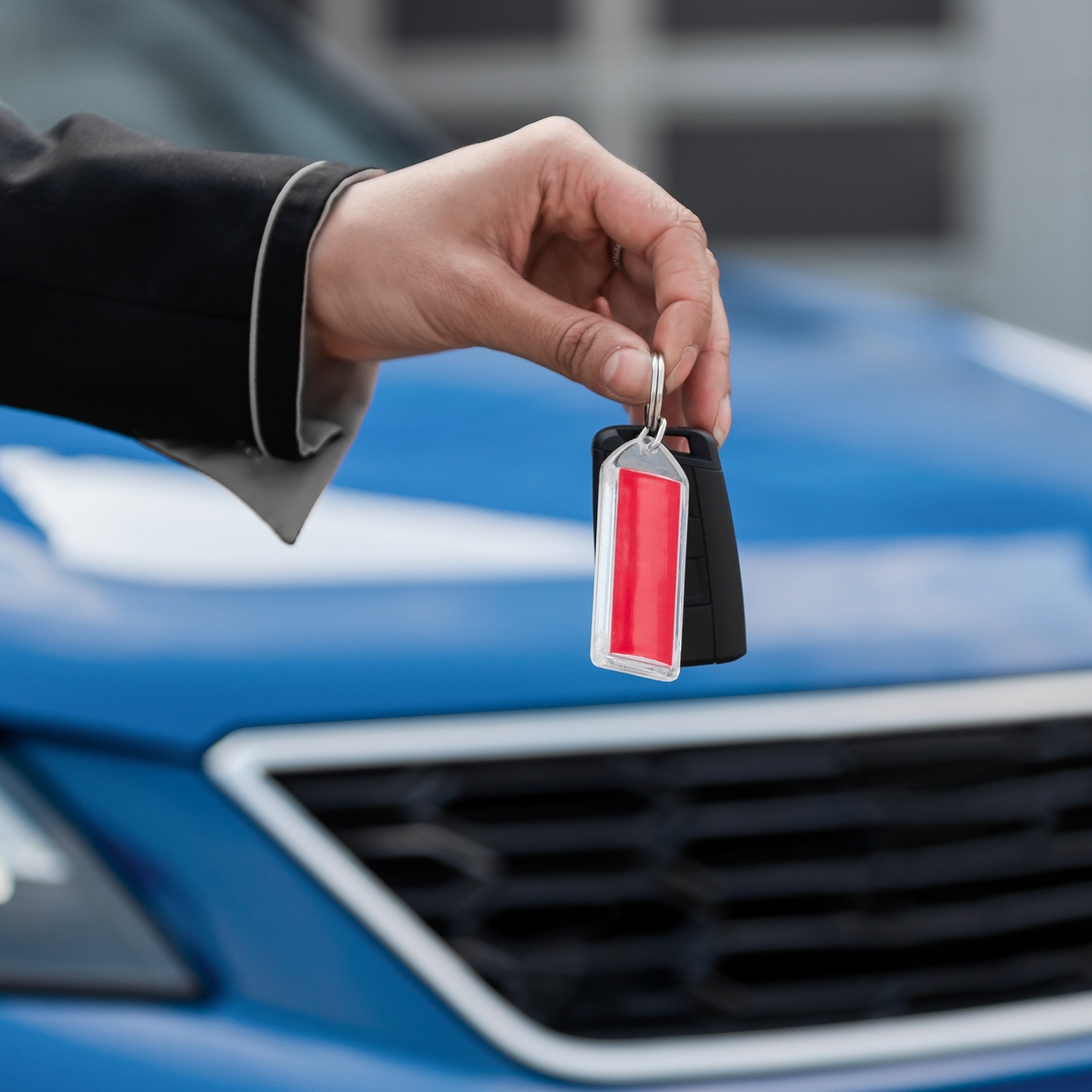 A woman holding out a set of car keys with a blue car in the background