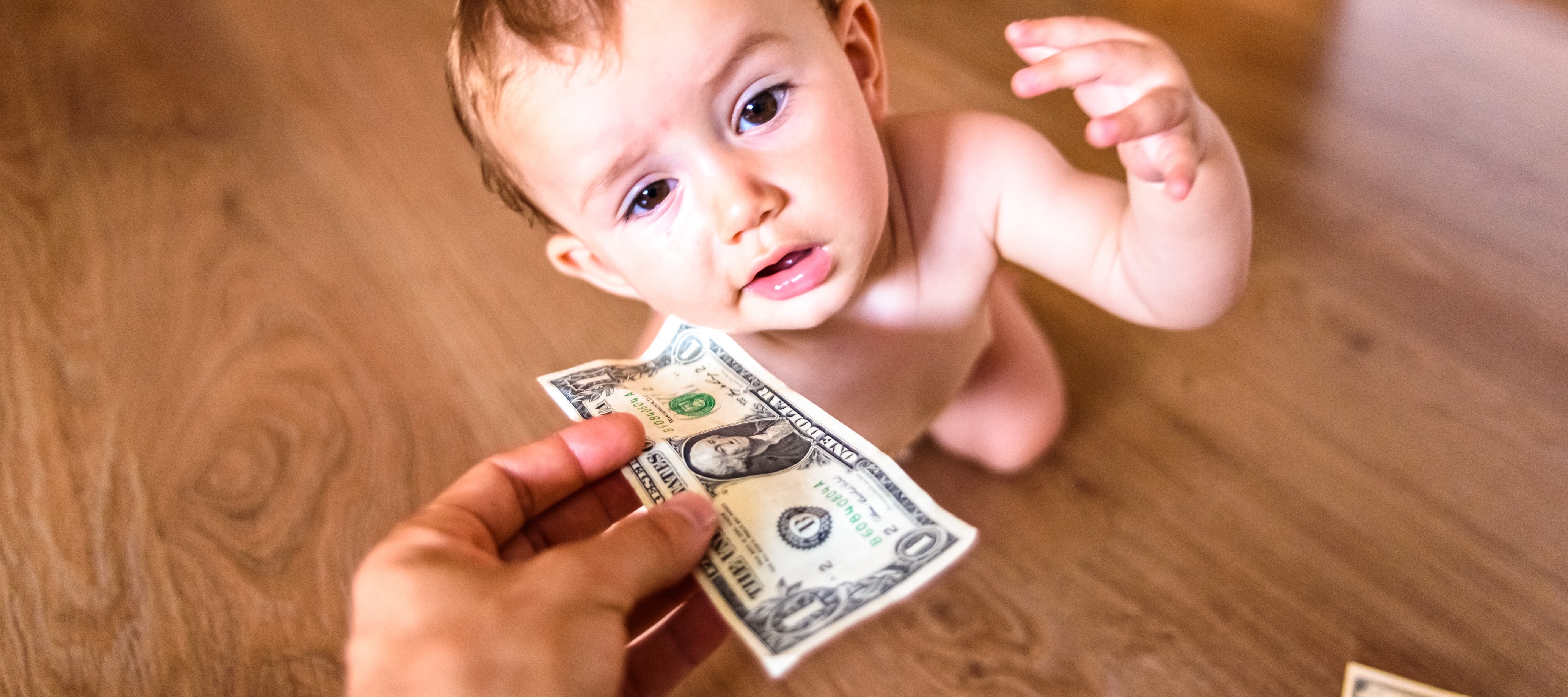 A toddler is the primary focus of this low angle shot, reaching for a dollar bill held out of frame.