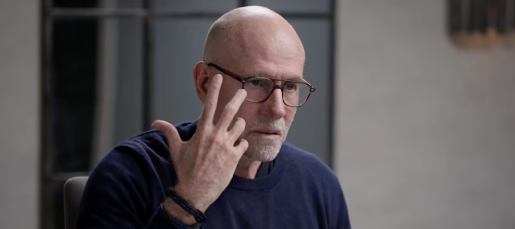 Scott Galloway, AKA Prof G, raises a hand with all five fingers spread, looking grim.