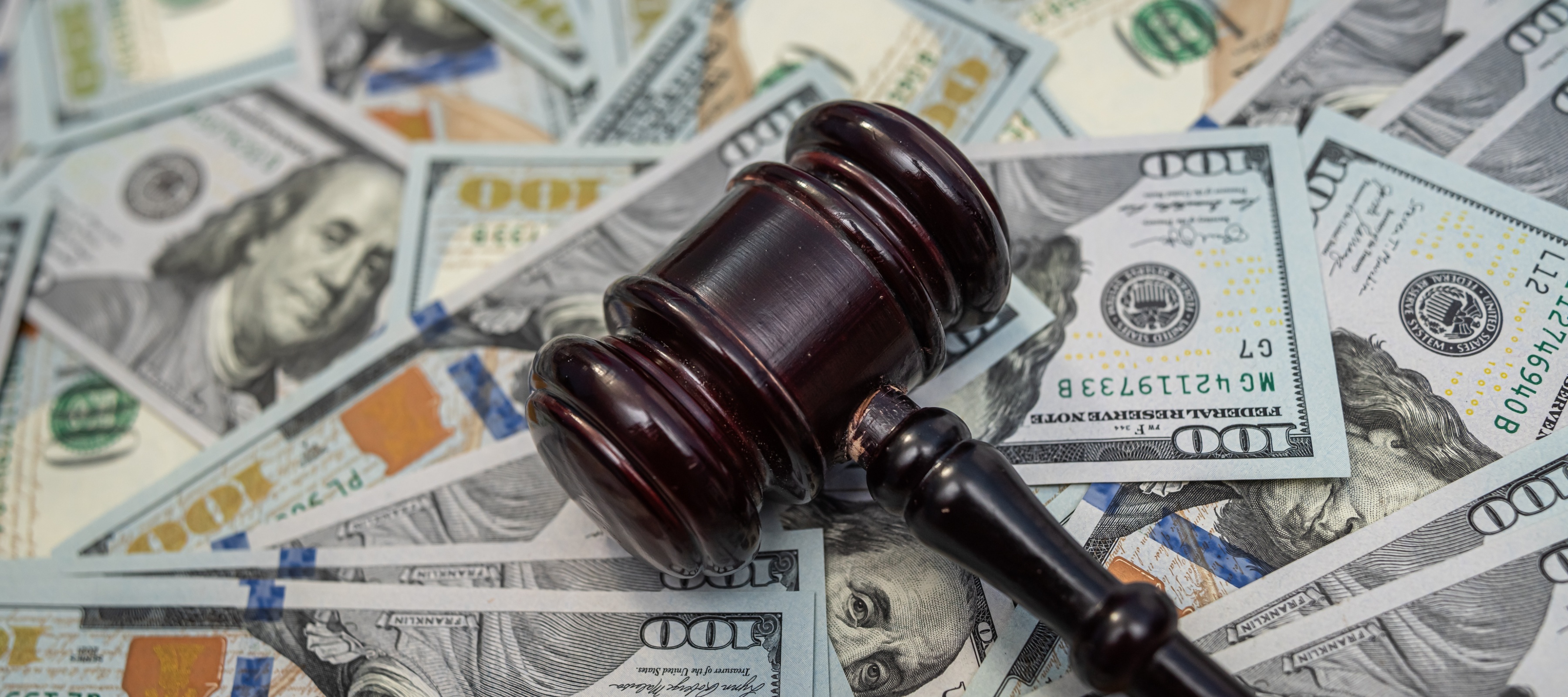 A pile of $100 bills is seen with a judge's gavel.