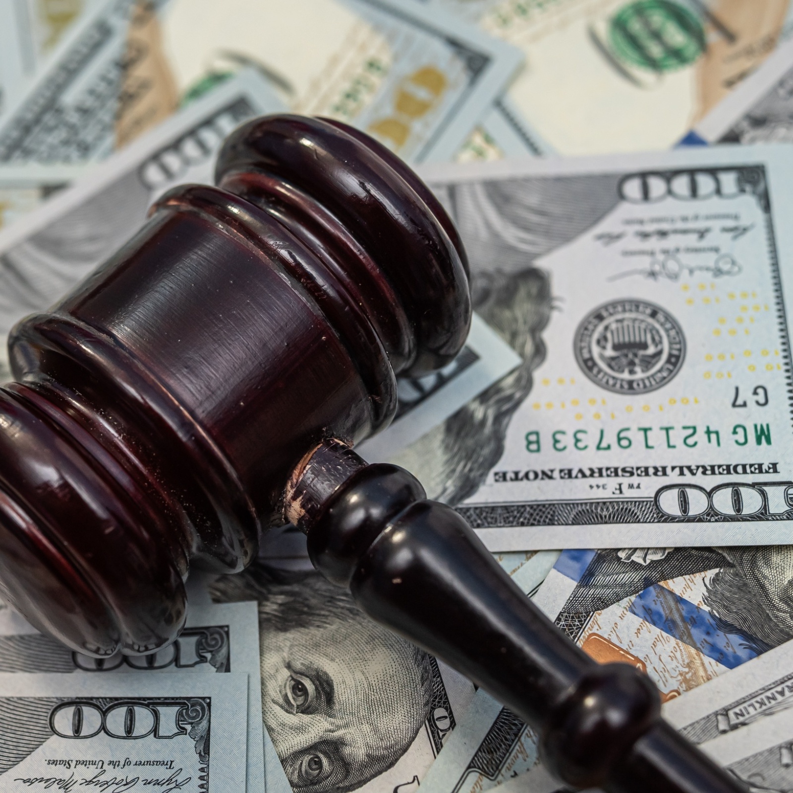 A pile of $100 bills is seen with a judge's gavel.
