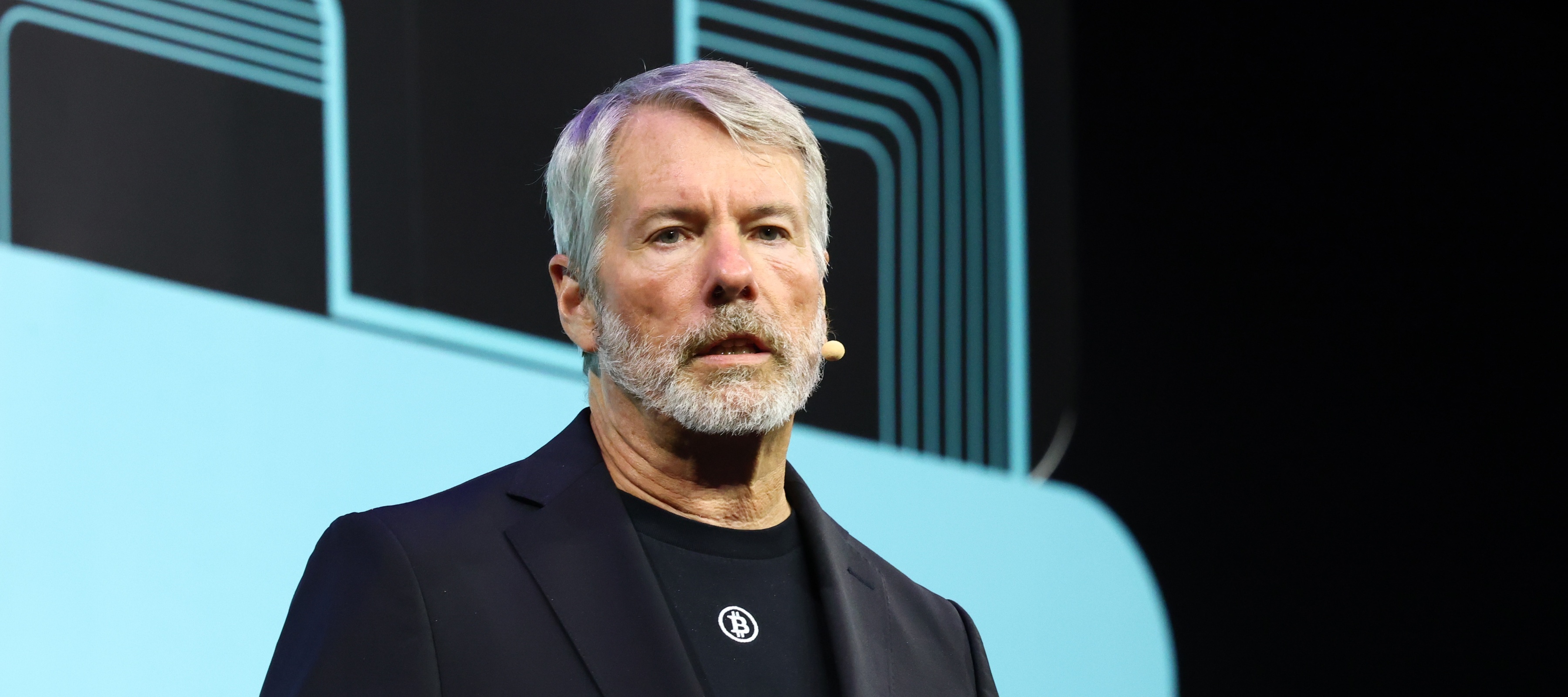 Michael Saylor wearing a black bitcoin shirt on stage giving a speech