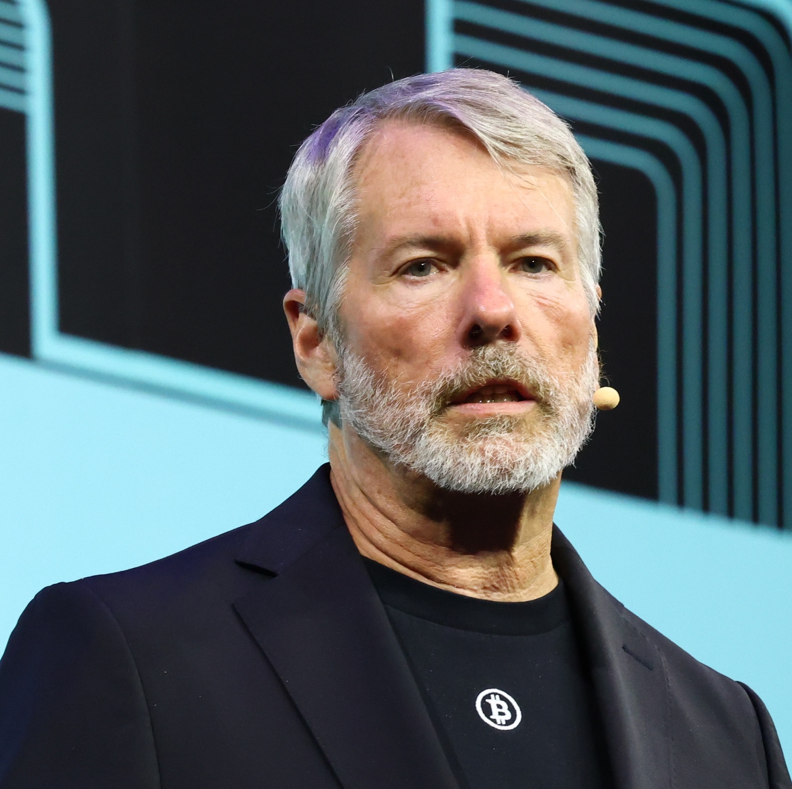 Michael Saylor wearing a black bitcoin shirt on stage giving a speech