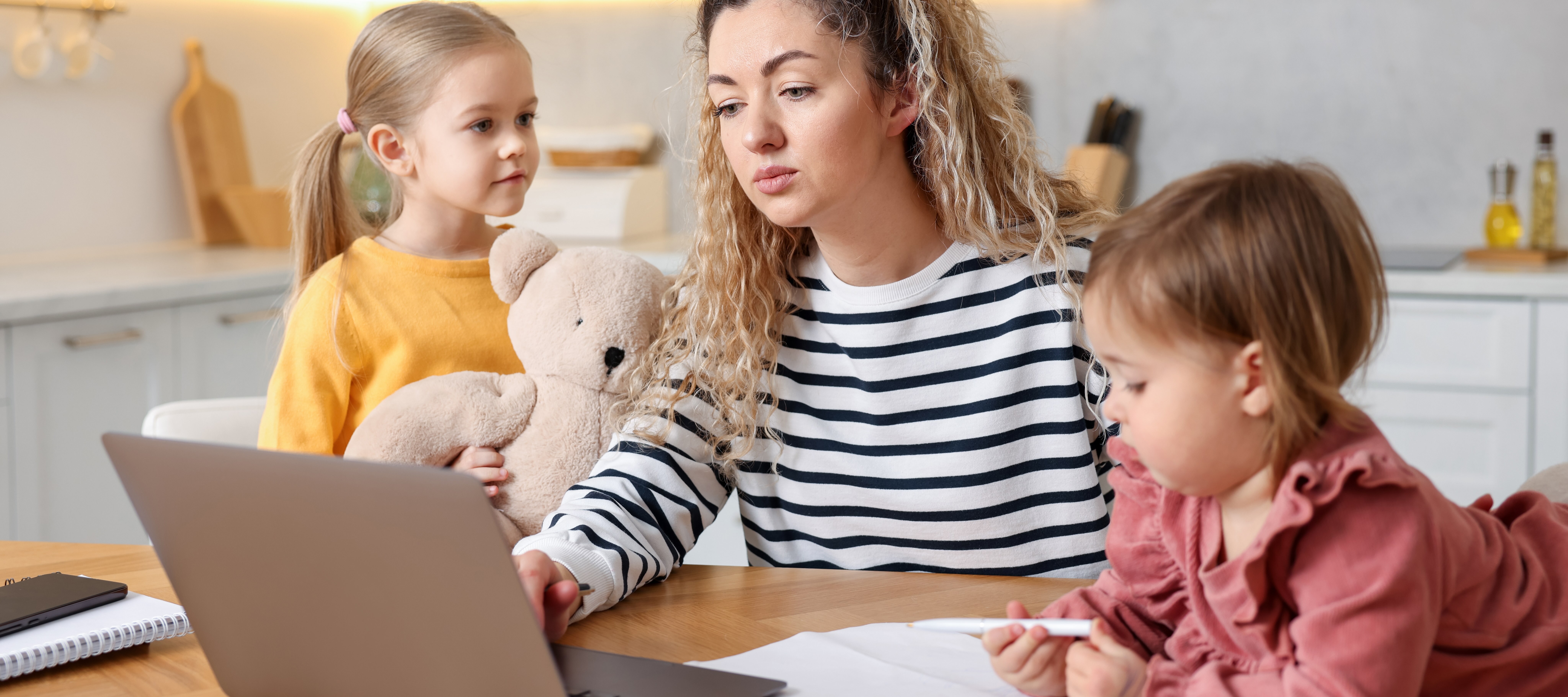 Mom looking at taxes on laptop with two young daughters