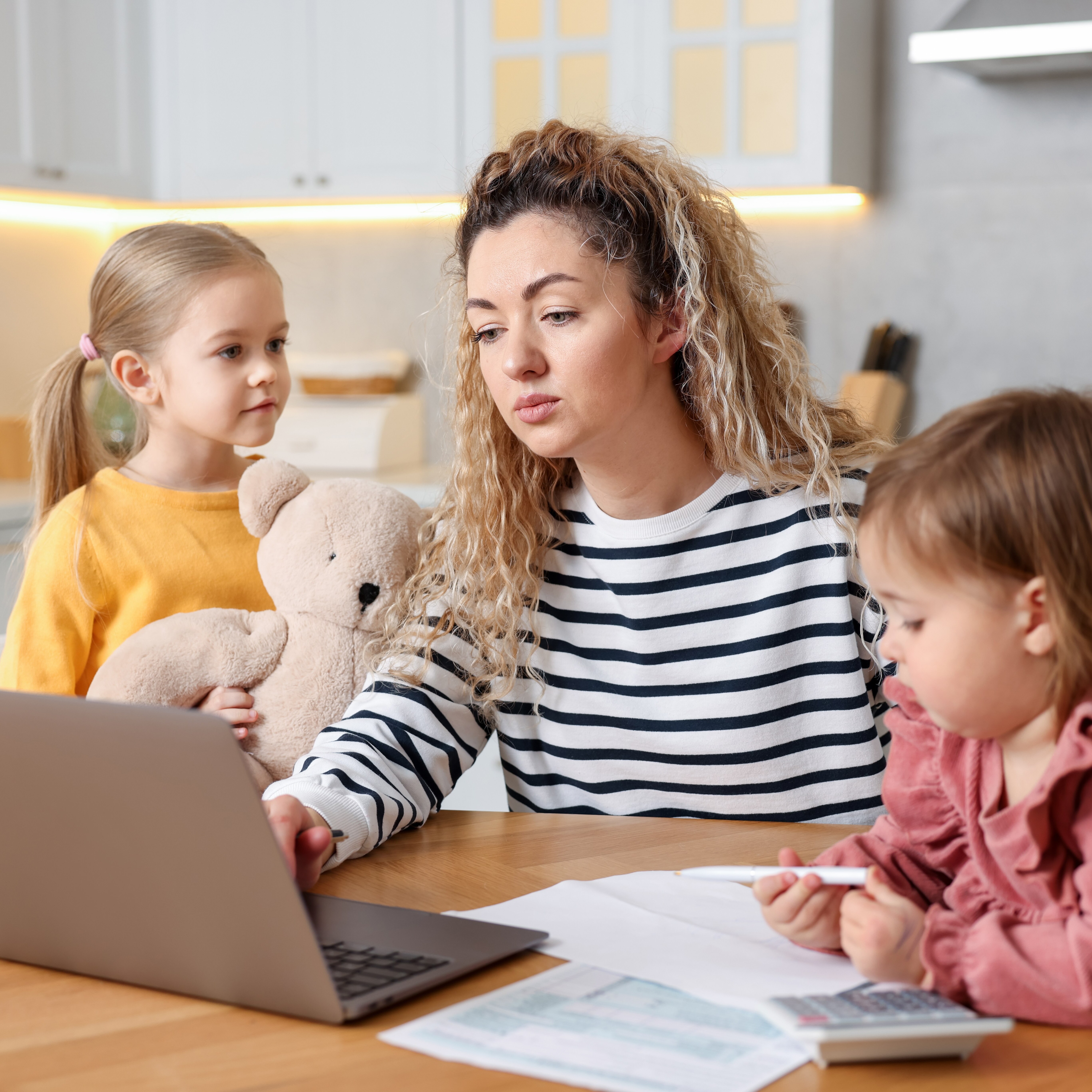 Mom looking at taxes on laptop with two young daughters