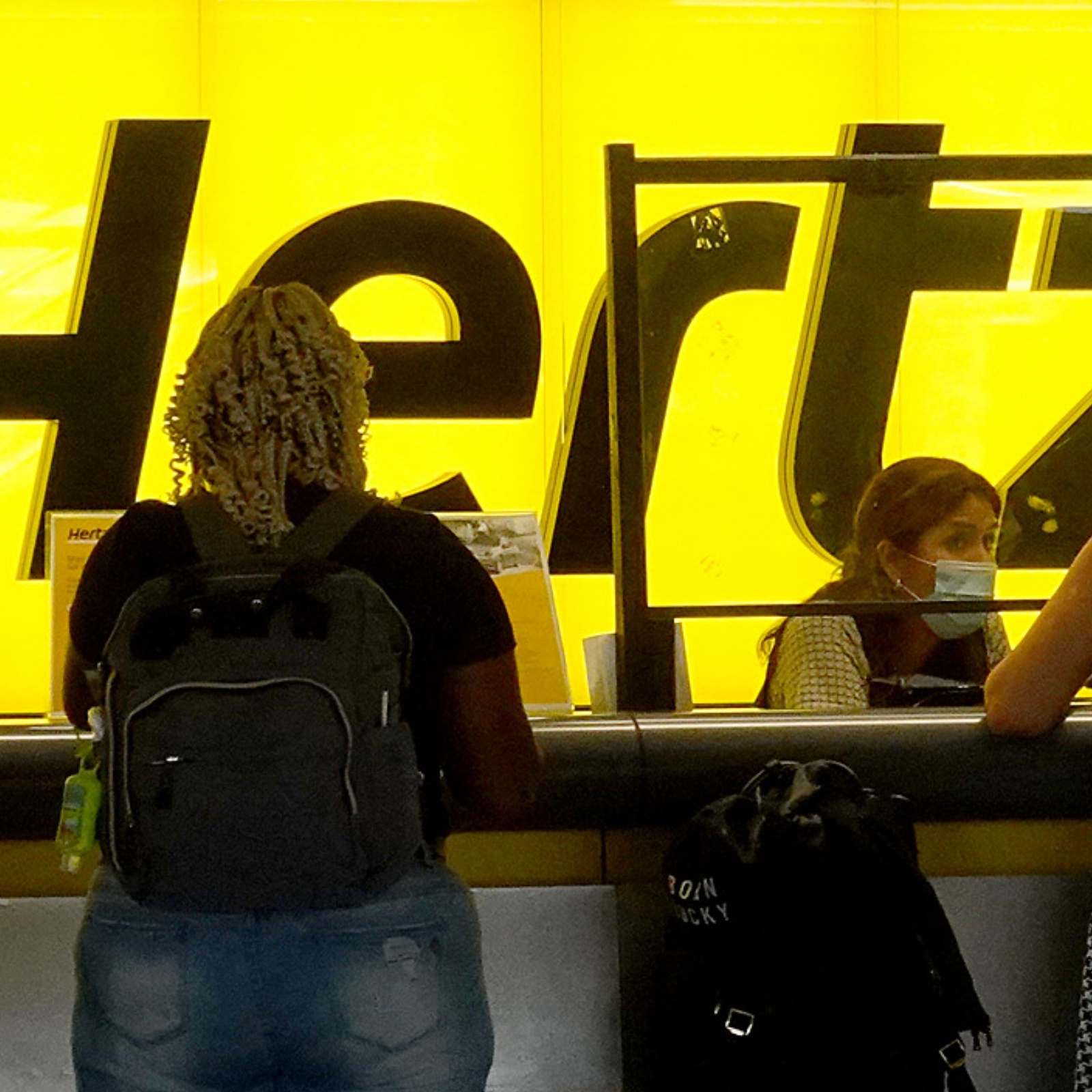 Three people stand in front of a brightly lit Hertz counter at an airport