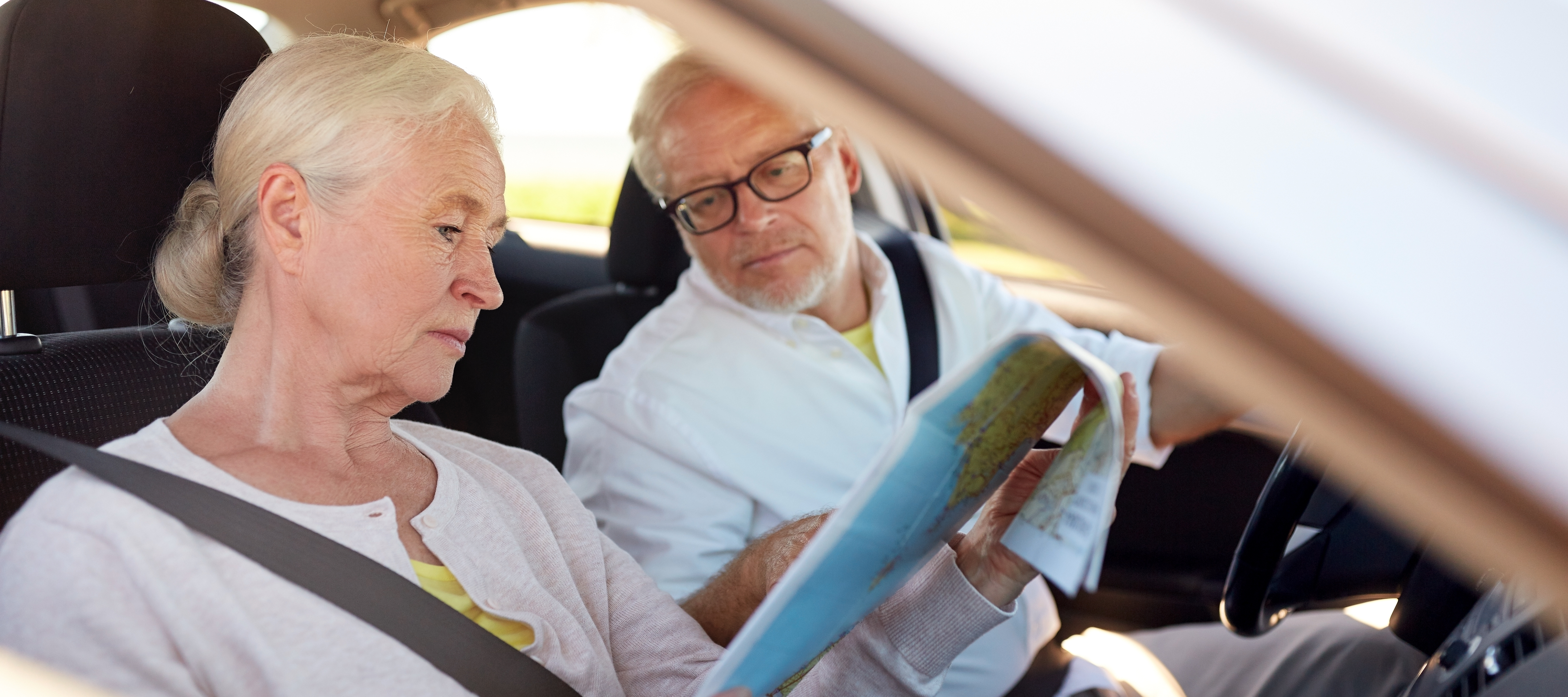 An older couple sits in a car looking at a map.