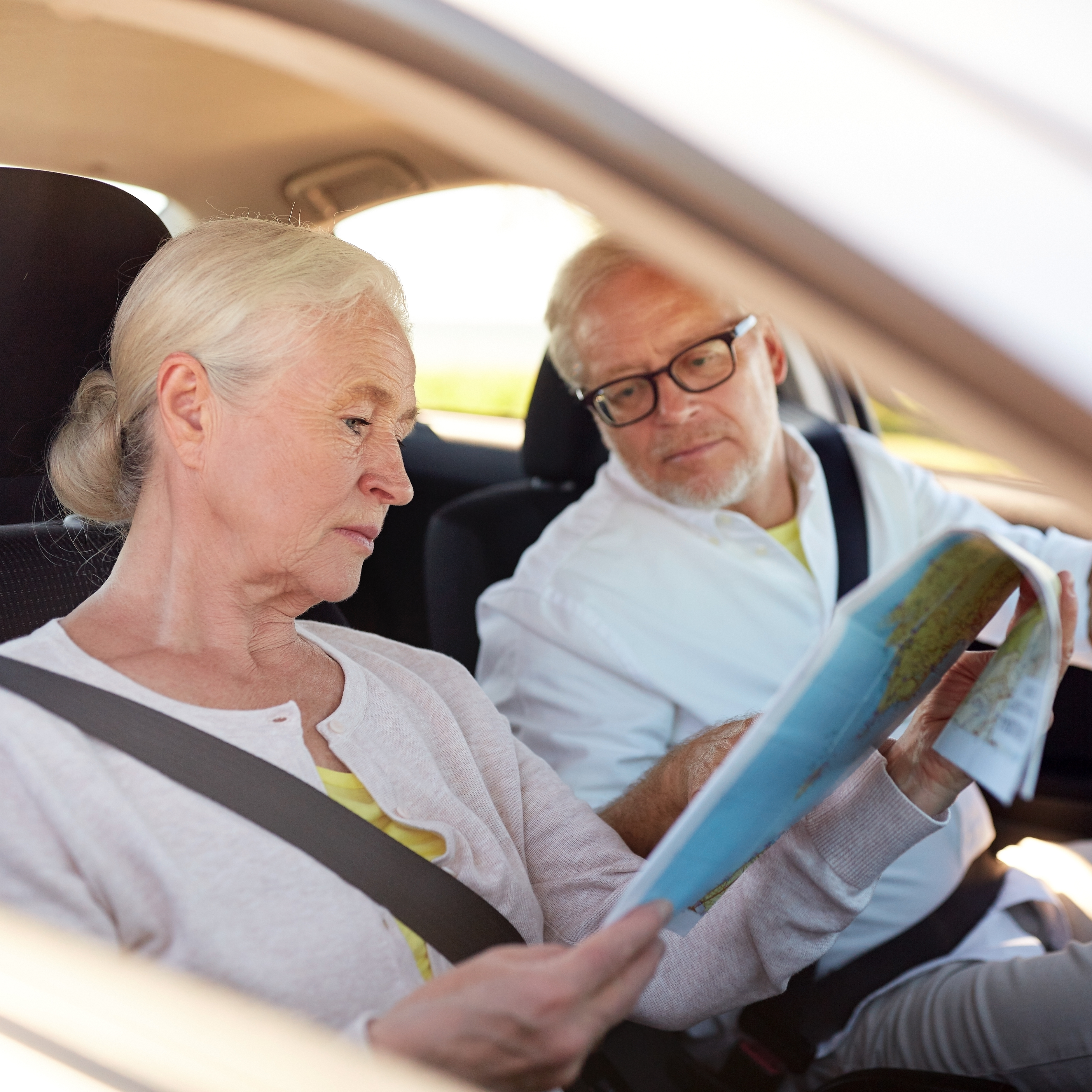 An older couple sits in a car looking at a map.