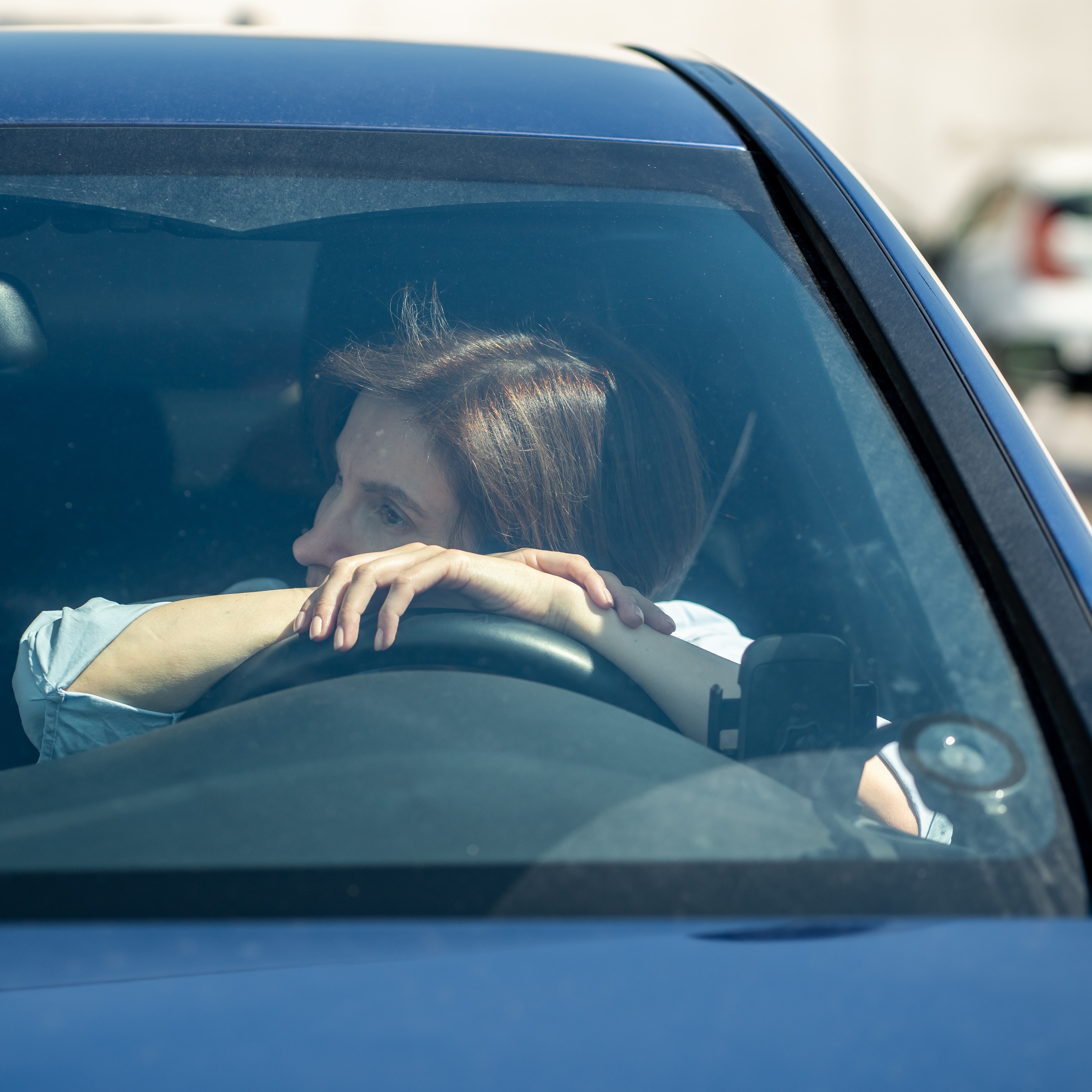 Young woman tiredly leaning on steering wheel