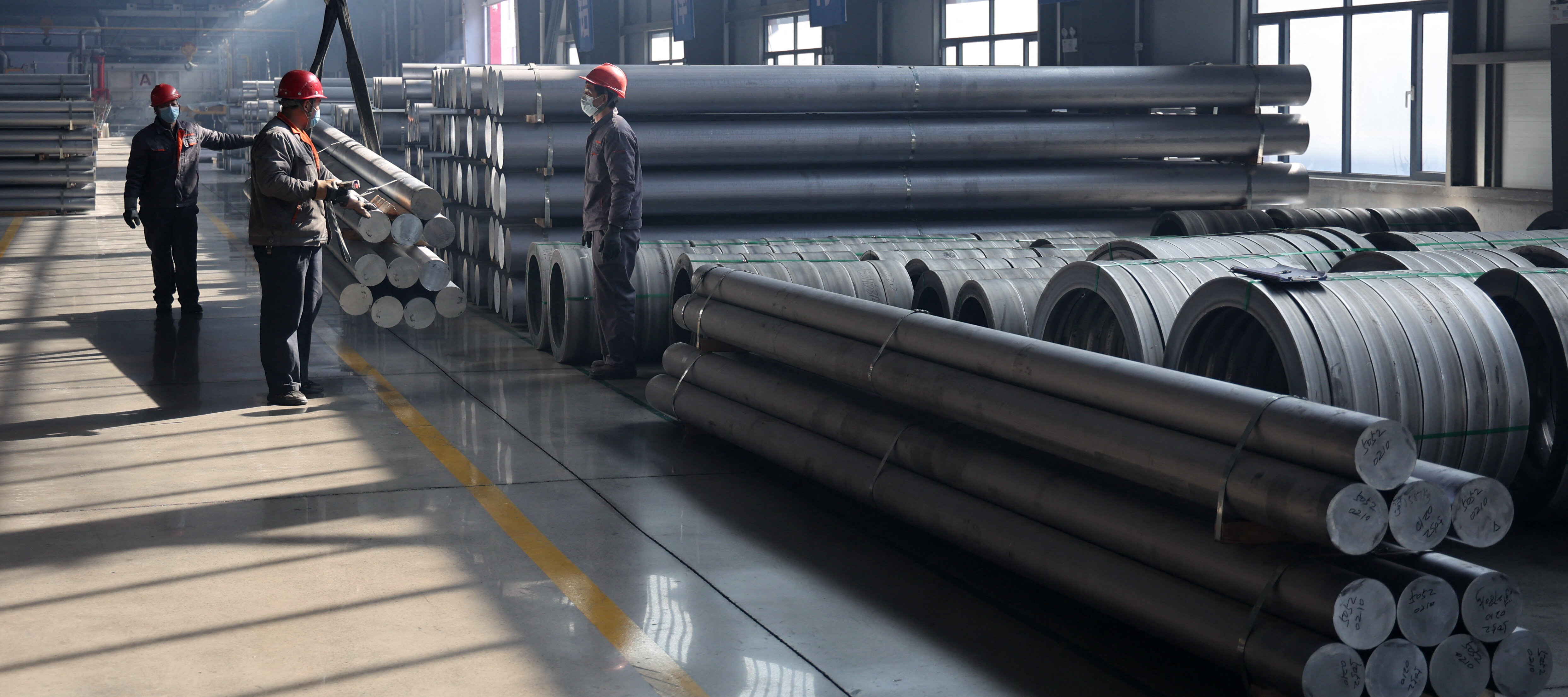 Workers transporting aluminium rods at an aluminium-base material factory.