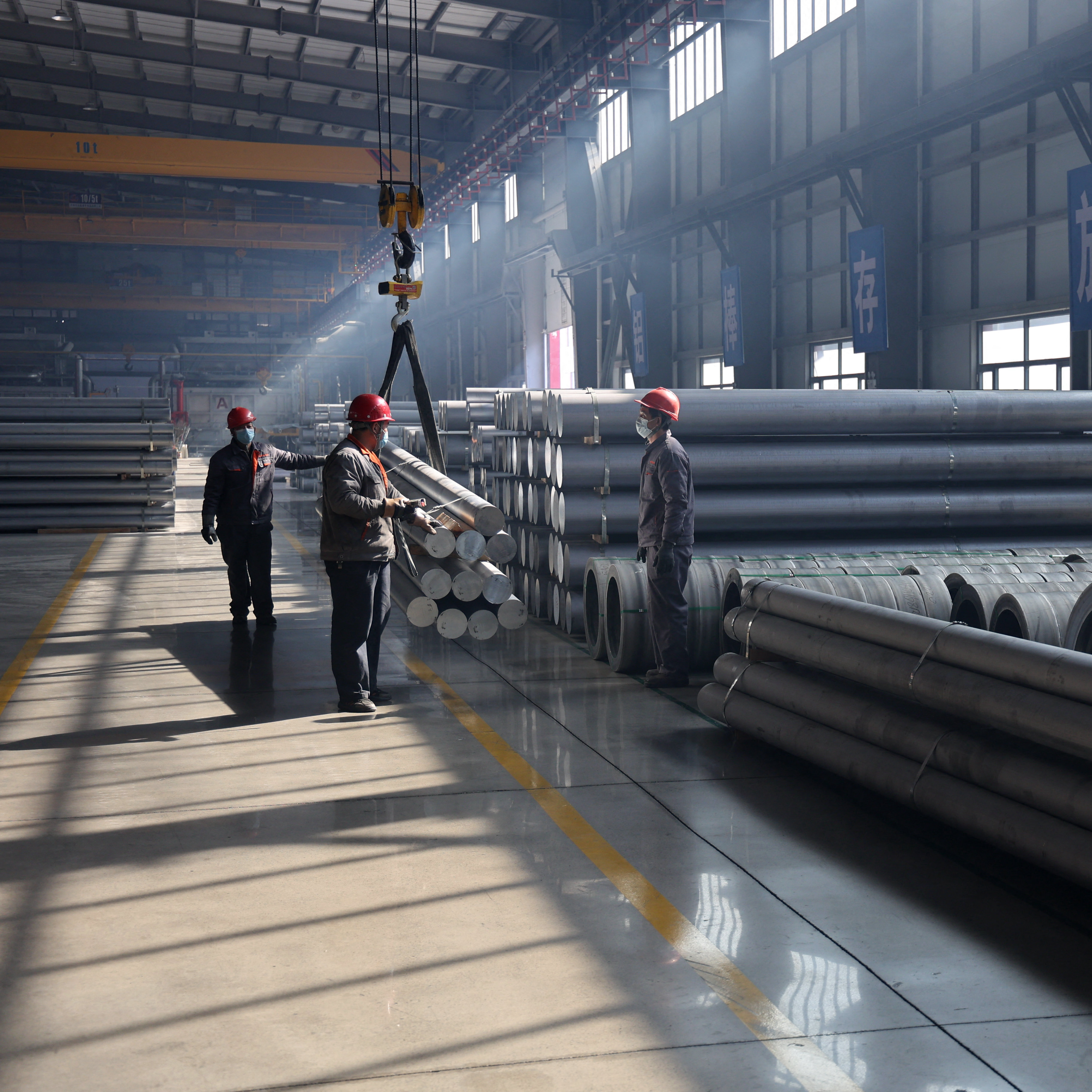 Workers transporting aluminium rods at an aluminium-base material factory.
