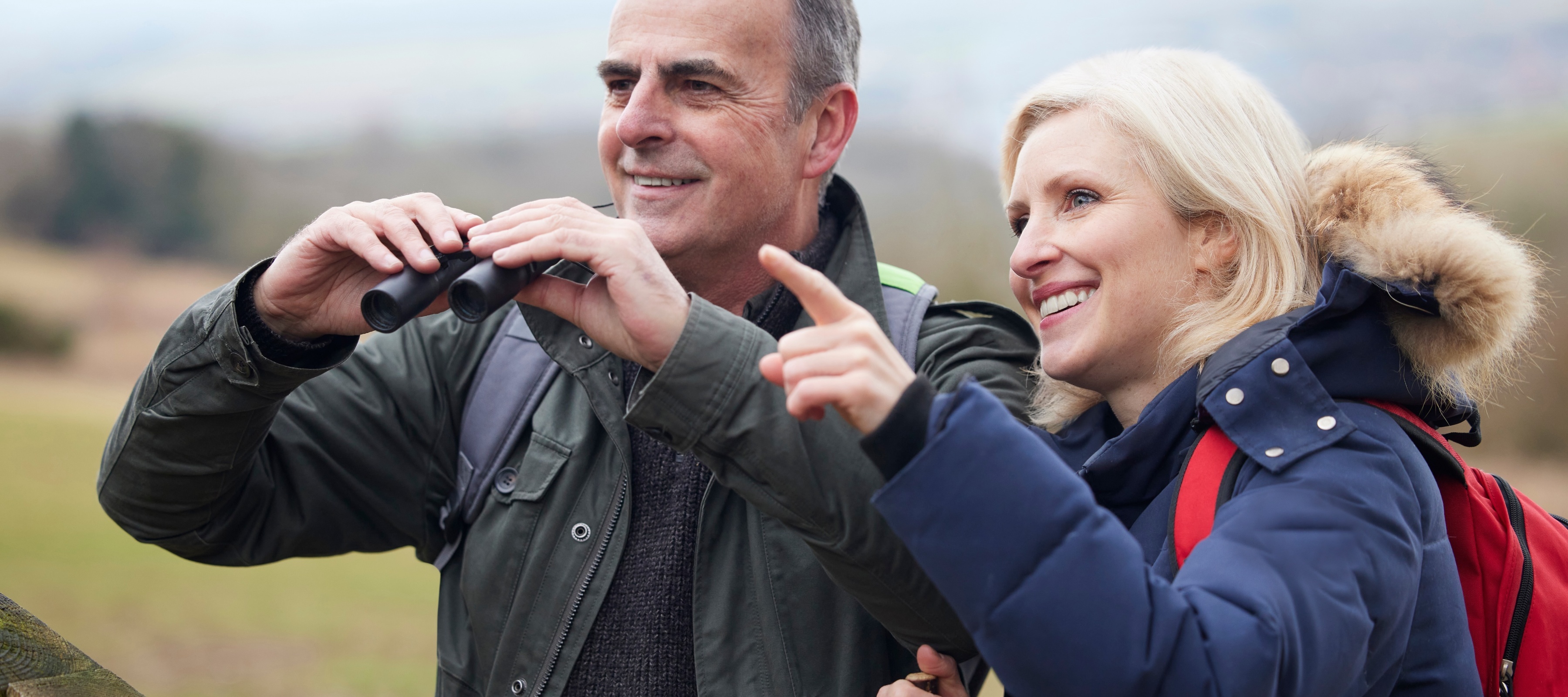 A mature couple on a hike are smiling as they look at wildlife.