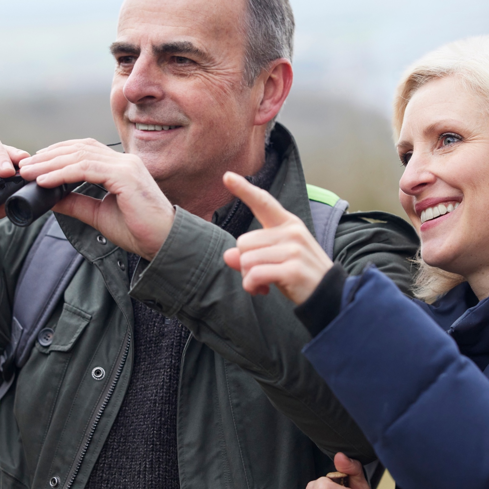 A mature couple on a hike are smiling as they look at wildlife.