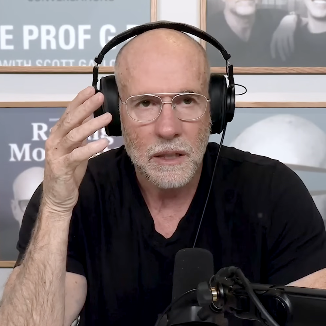 A close-up of Scott Galloway talking on his podcast about the transition of wealth while wearing a black t-shirt and over-ear headphones.