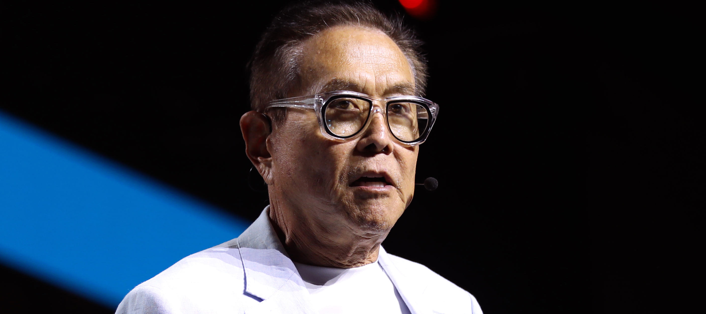 Robert Kiyosaki stands on stage in a white suit.