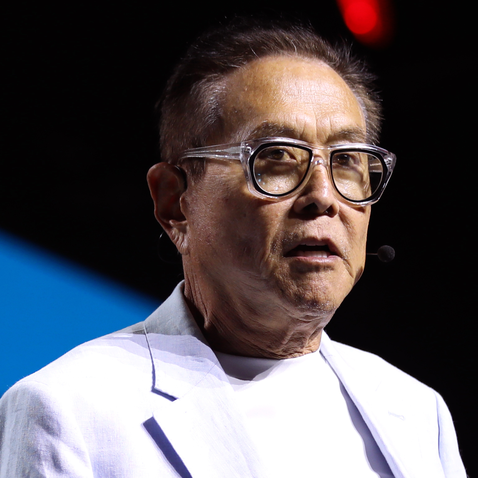Robert Kiyosaki stands on stage in a white suit.