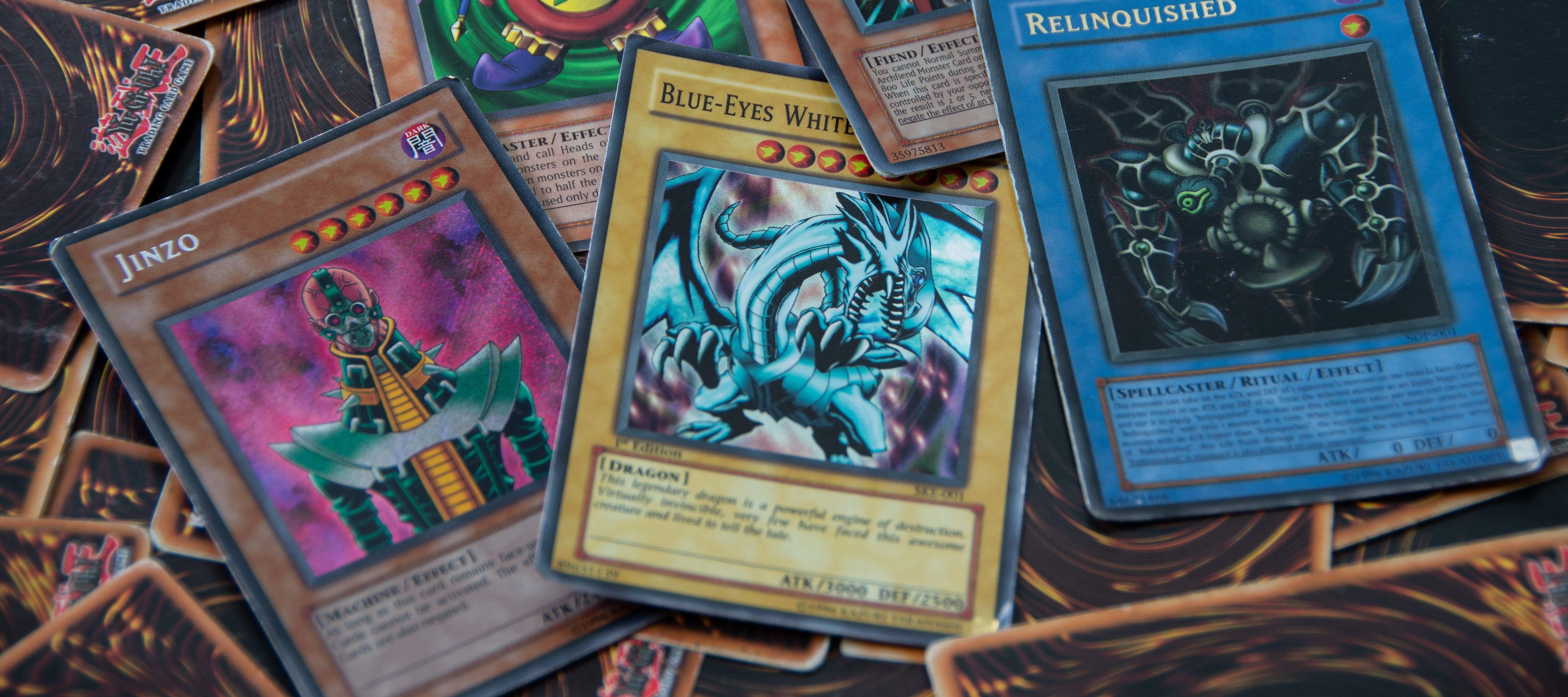 A close up of a few face-up Yu-Gi-Oh! cards spread across a pile of cards on a flat surface.