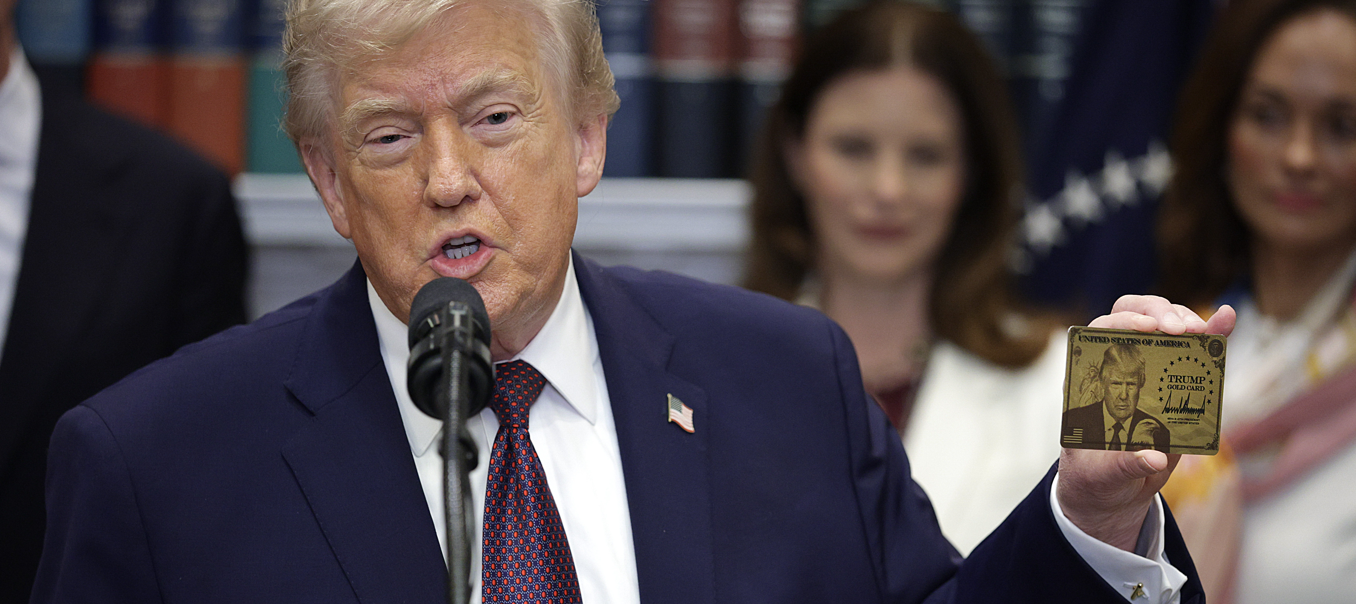 President Trump holds a "Trump Gold Card" during an event in the Roosevelt Room of the White House.