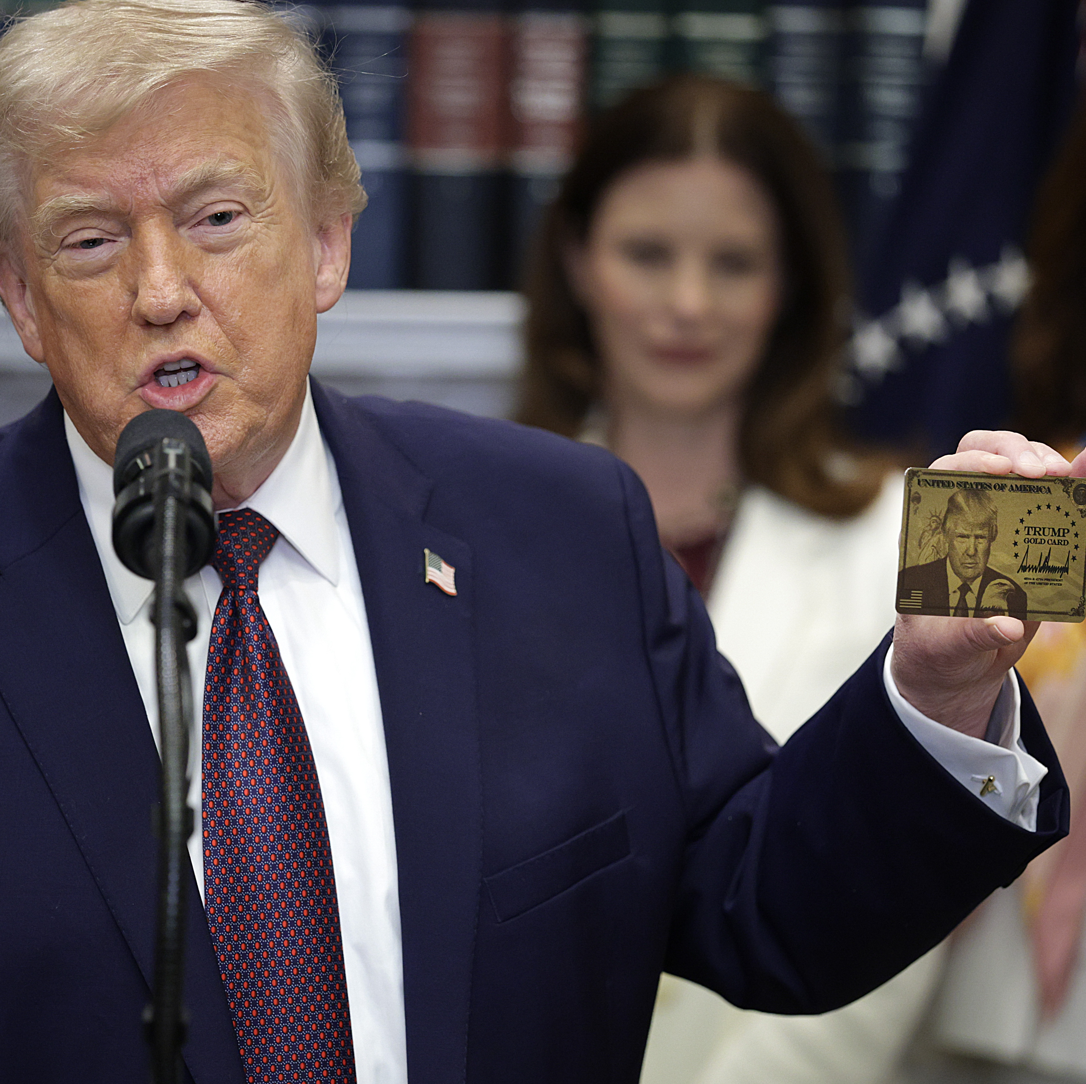 President Trump holds a "Trump Gold Card" during an event in the Roosevelt Room of the White House.