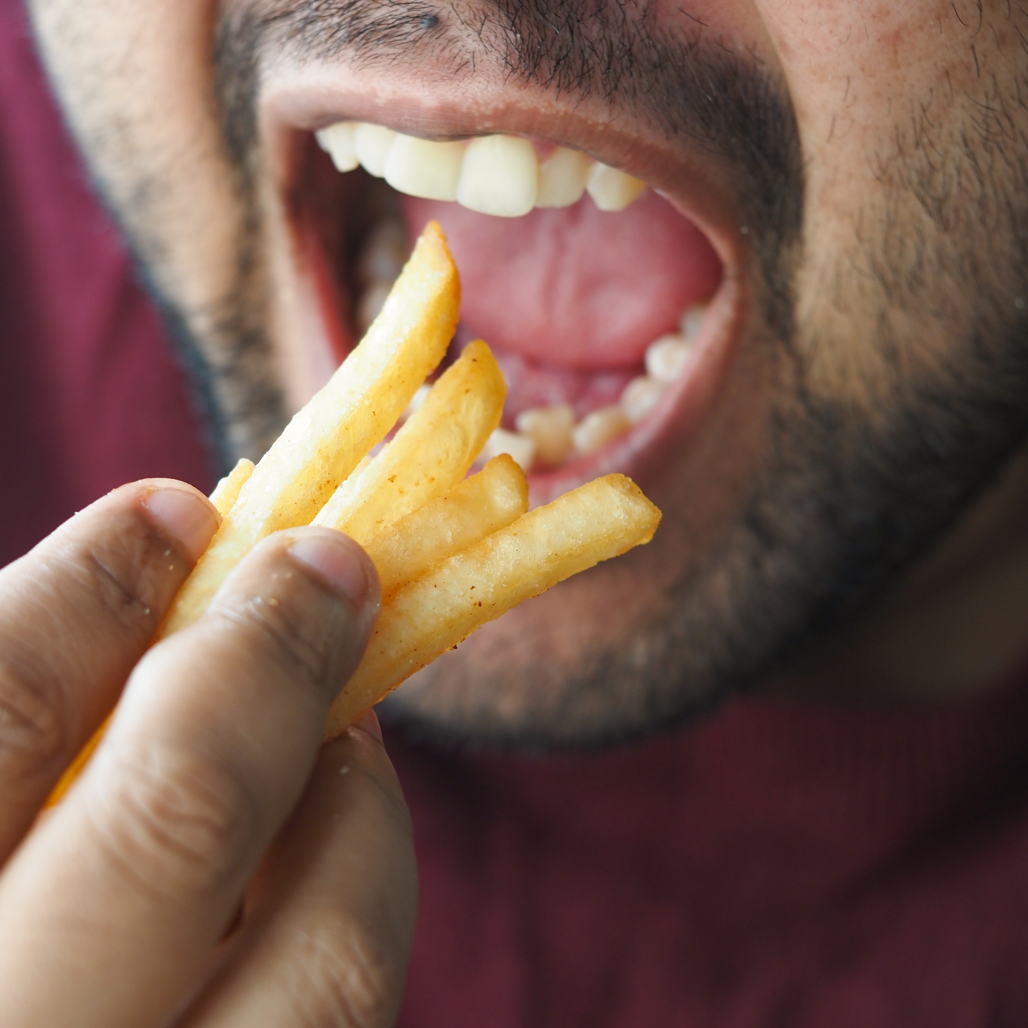 A close up of a man's mouth as he eats a handful of french fries.