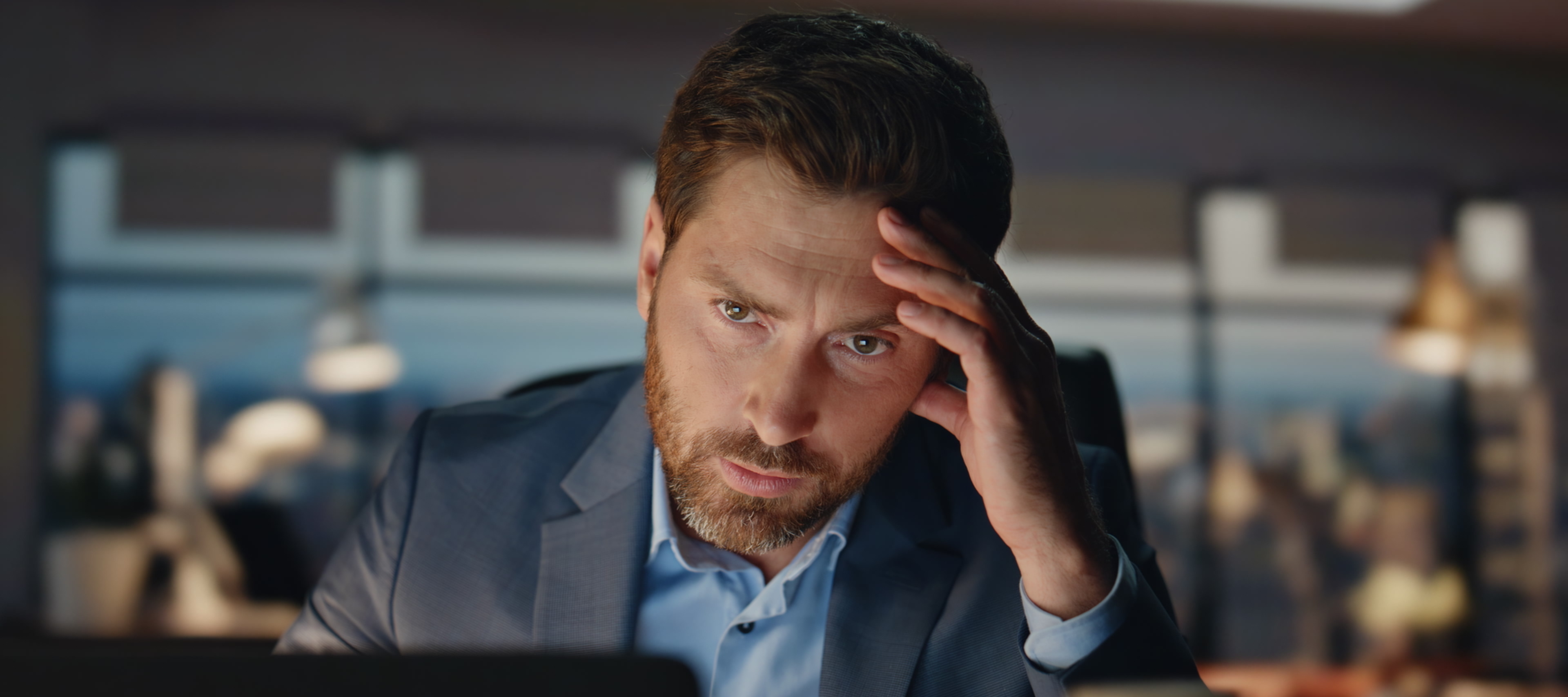 Close up shot shows a man in a suit looking stressed in an office environment.