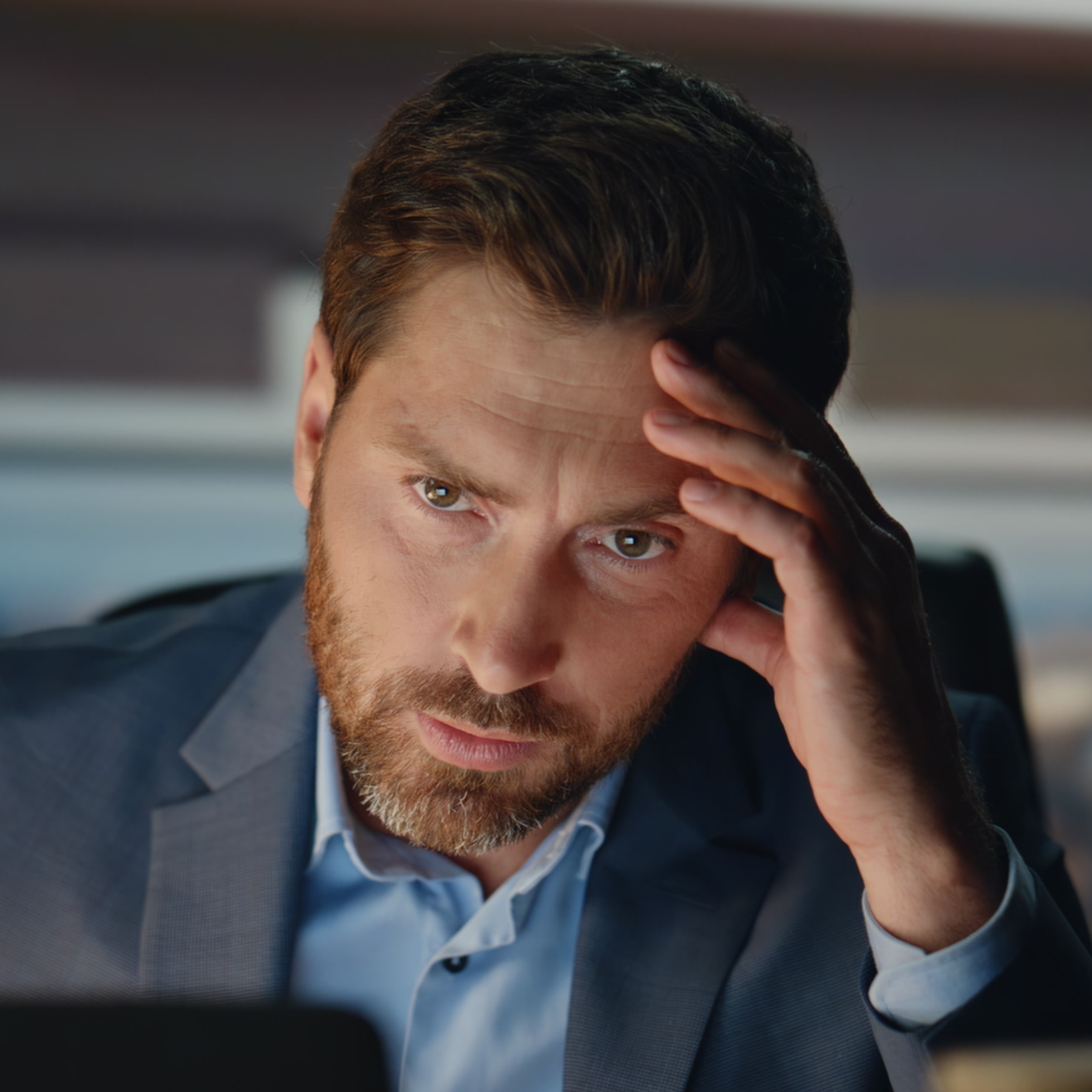 Close up shot shows a man in a suit looking stressed in an office environment.