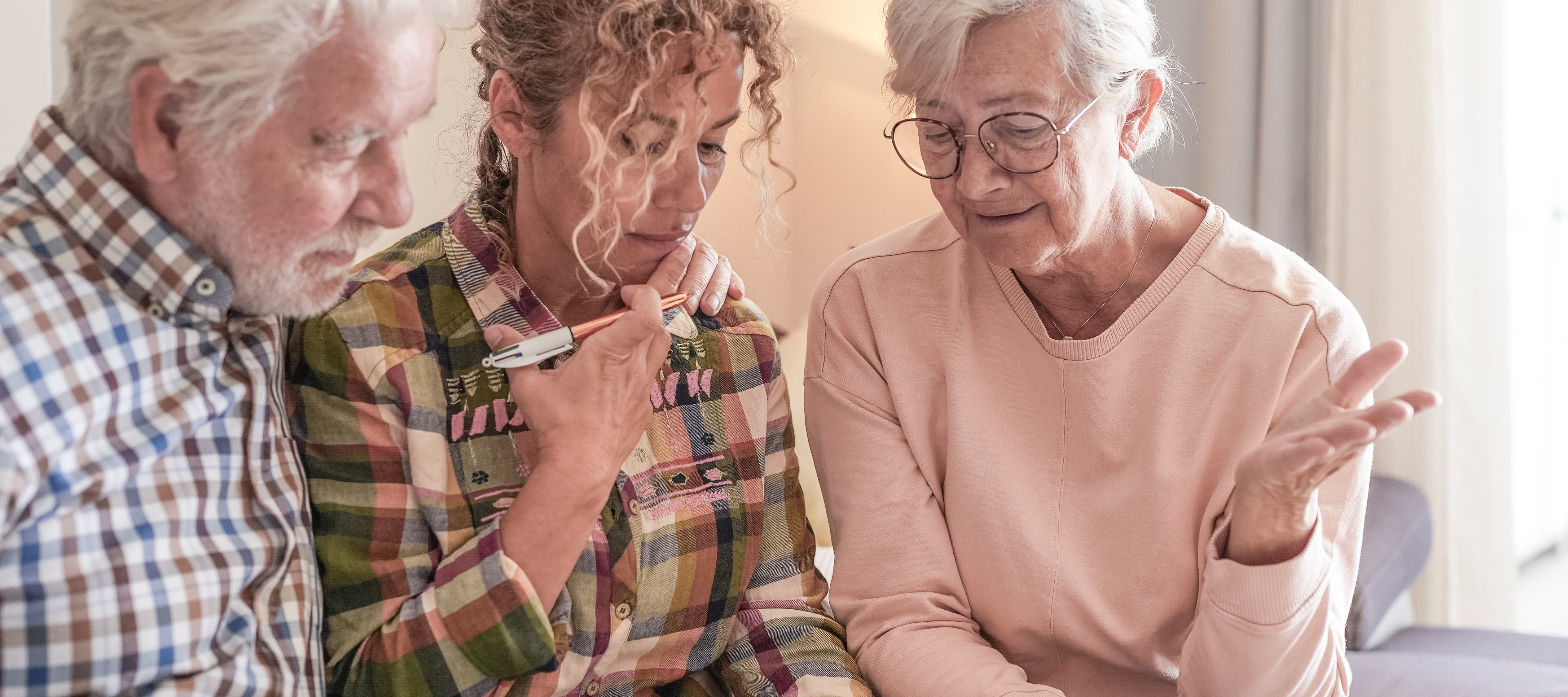 Retired couple sitting with their adult daughter, looking pensive
