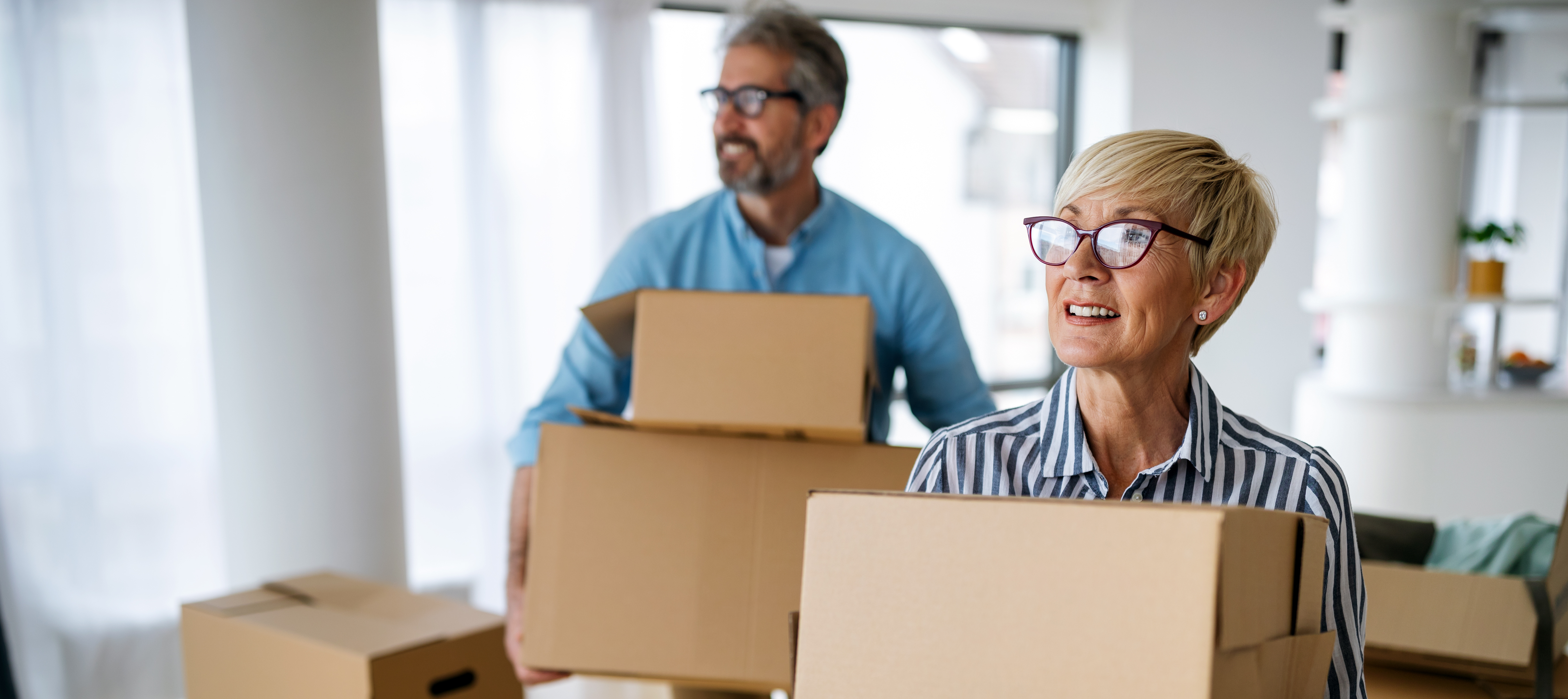 A mature couple hold moving boxes in their new home.