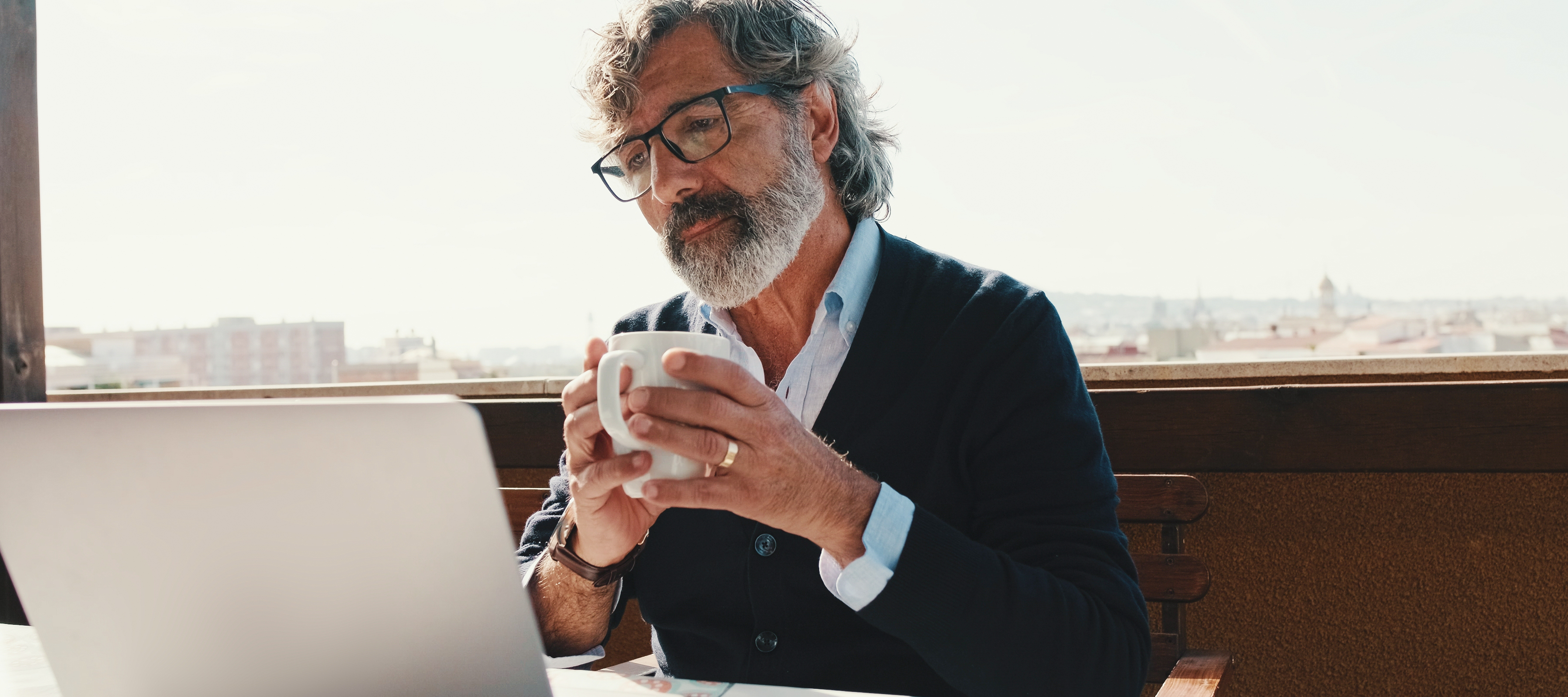 60-year-old man holding a mug and working on laptop