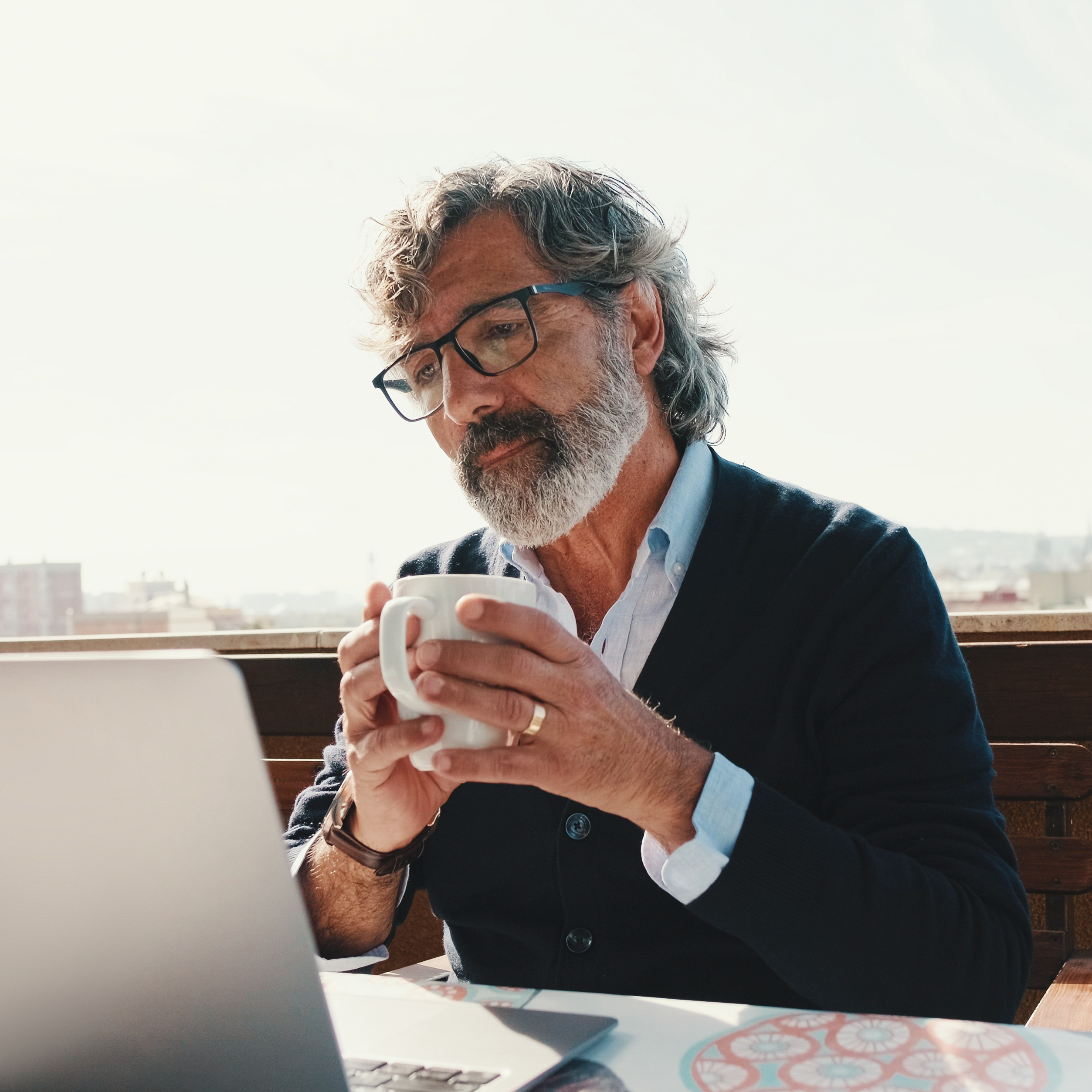 60-year-old man holding a mug and working on laptop