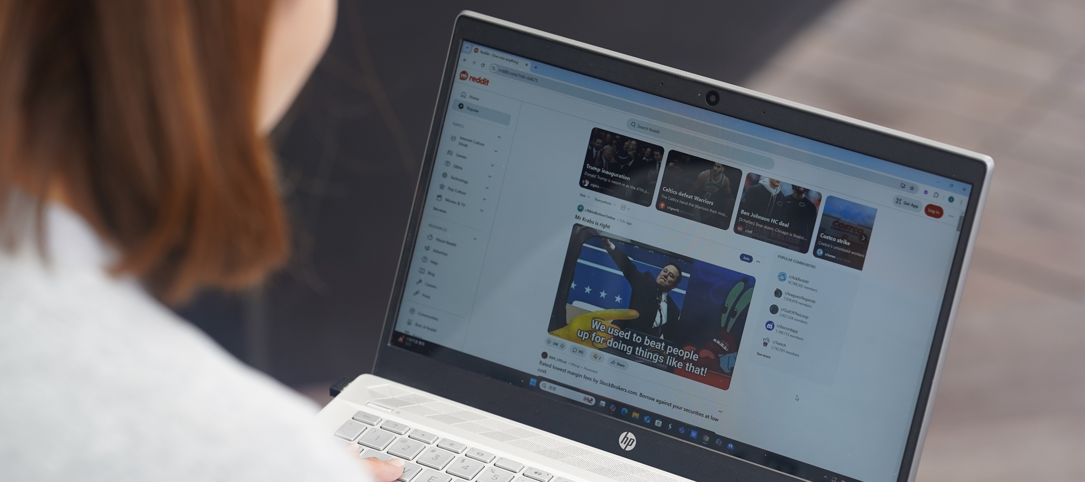 An over-the-shoulder view of a woman using Reddit on her laptop
